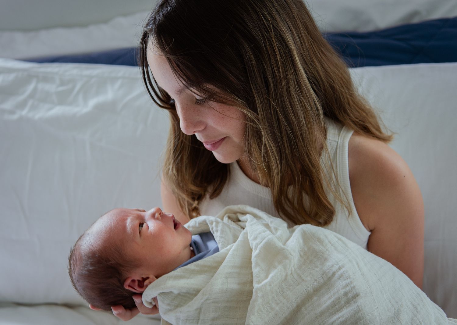 Series showing tender moments between parent and infant on white bedding.