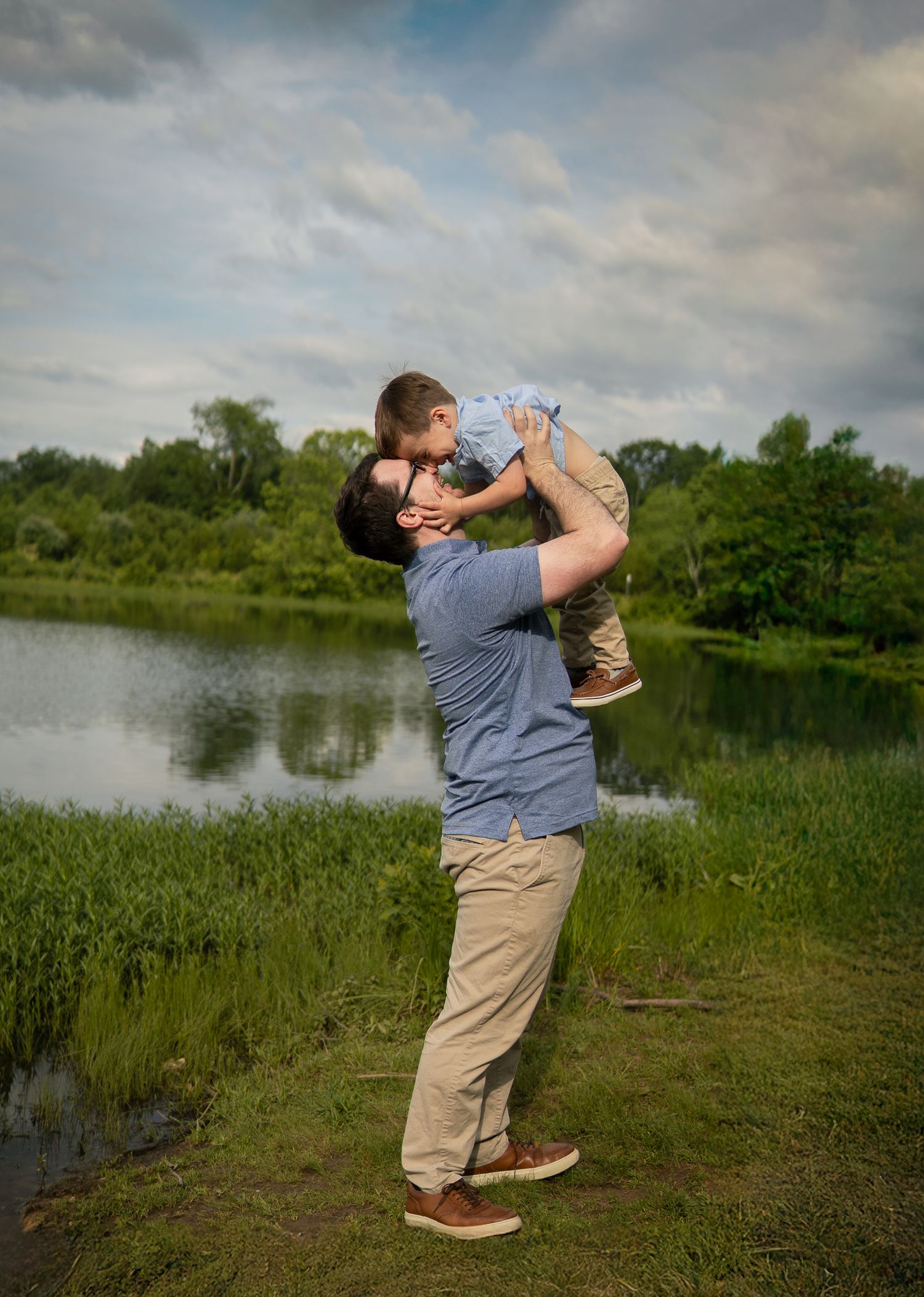 A tender interaction between adult and child beside a serene lake surrounded by lush greenery.
