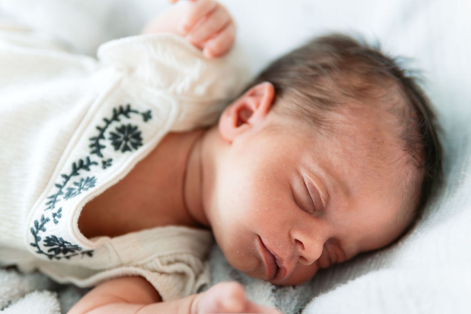 Newborn baby sleeping peacefully in white clothing against light background.