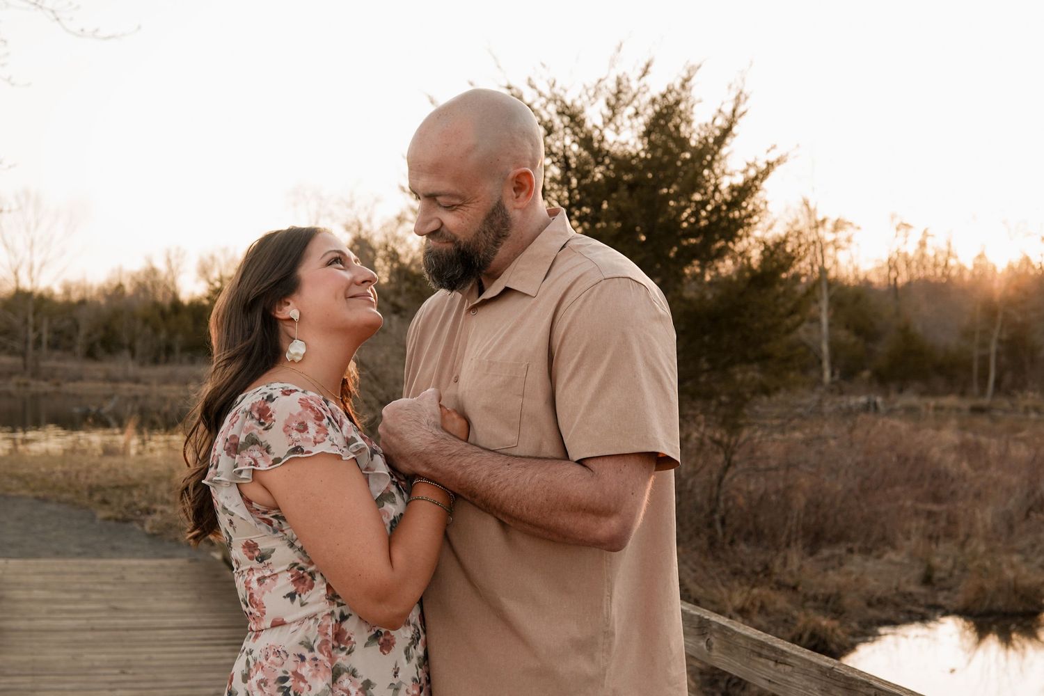 Couple sharing a tender moment on a wooden boardwalk at sunset with natural landscape in background.