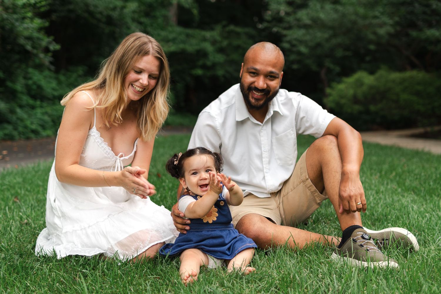 Family wearing white sits together on grass in outdoor setting sharing joyful moments during photo session.