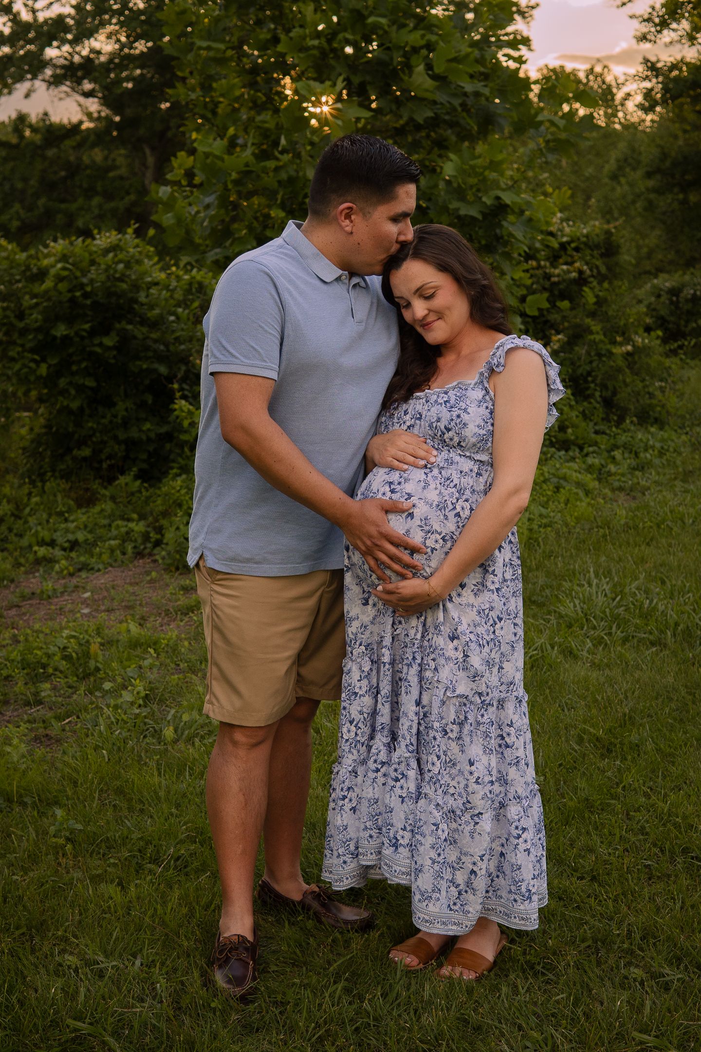 A couple shares an intimate moment outdoors at sunset as they lovingly embrace during a maternity photoshoot.