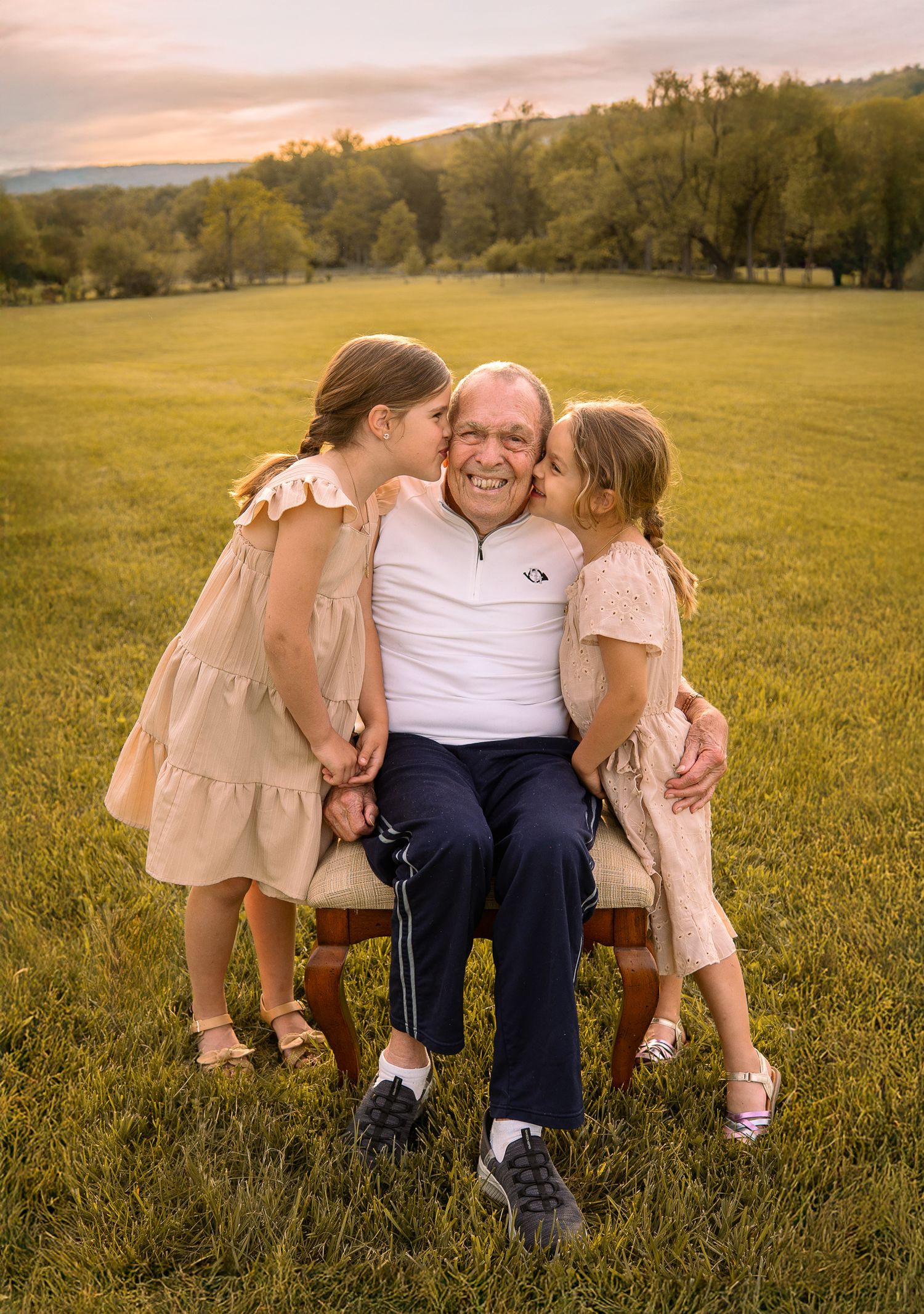 Family shares tender moment together sitting on grassy field at sunset with pink and golden lighting.