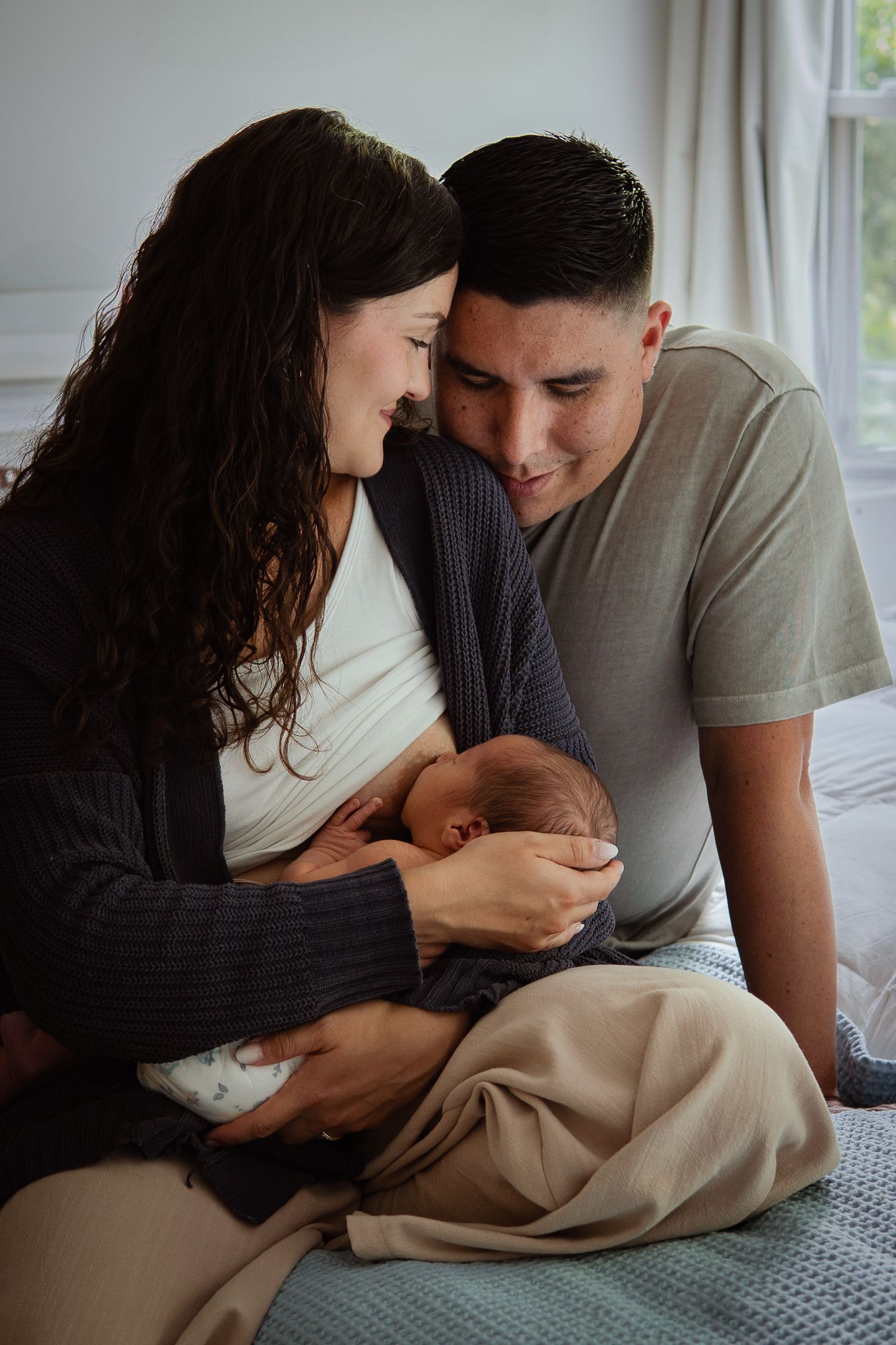 Series of intimate family moments with parents lovingly gazing at their newborn on bed.
