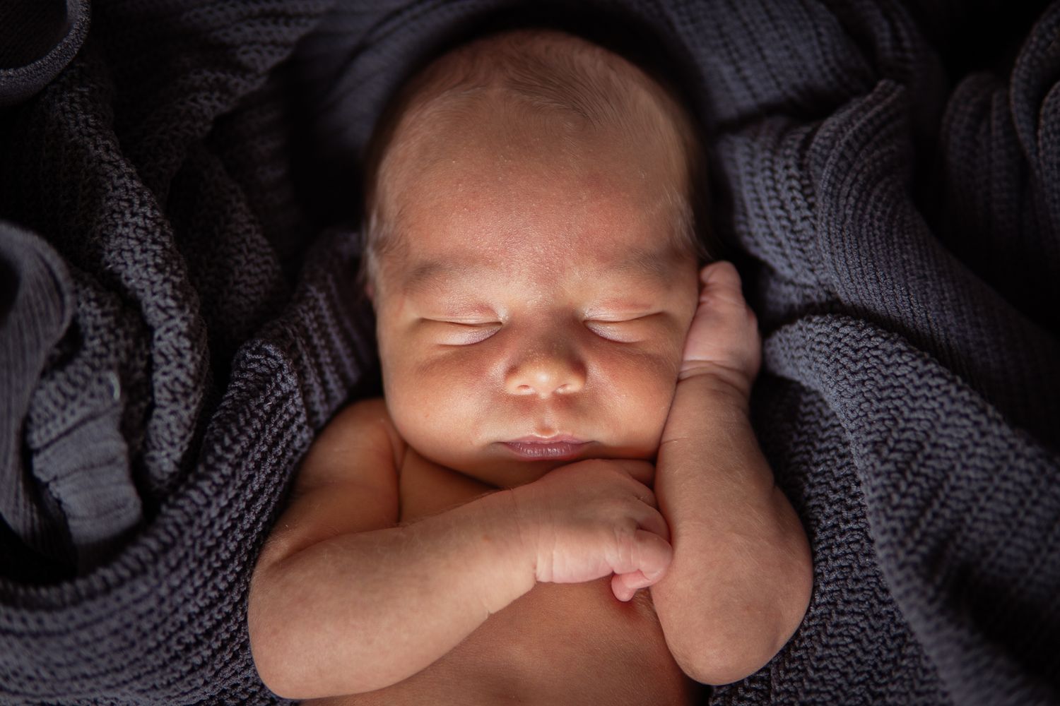 Peaceful newborn infant sleeping while wrapped in cozy gray knit blanket.