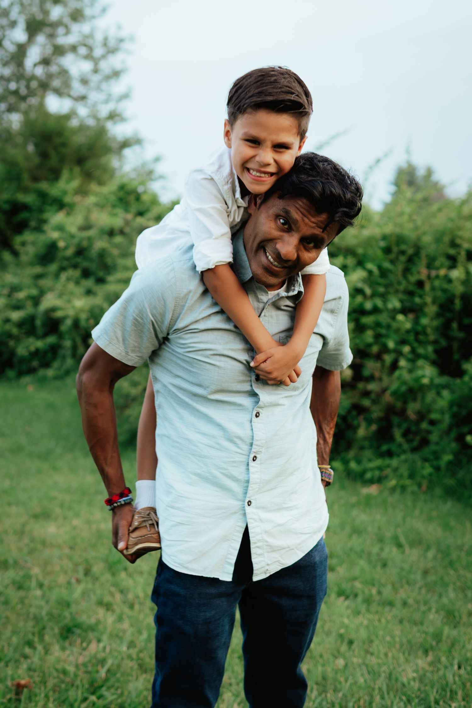 Playful piggyback ride sequence outdoors with two people in casual attire against greenery.