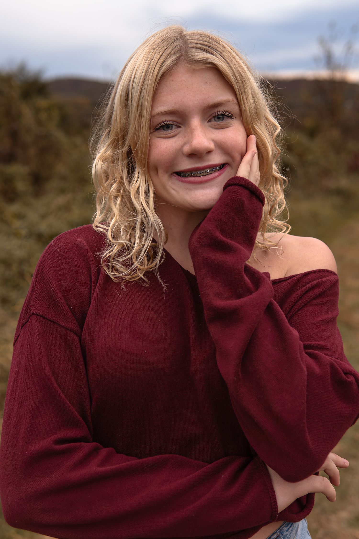 Person wearing a burgundy sweater poses playfully outdoors on a sunny autumn day.