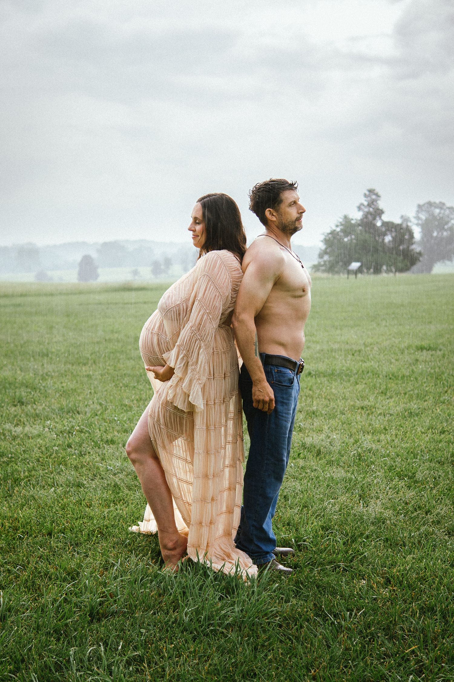 A couple poses back-to-back in a misty field, with the woman in a flowing peach dress.