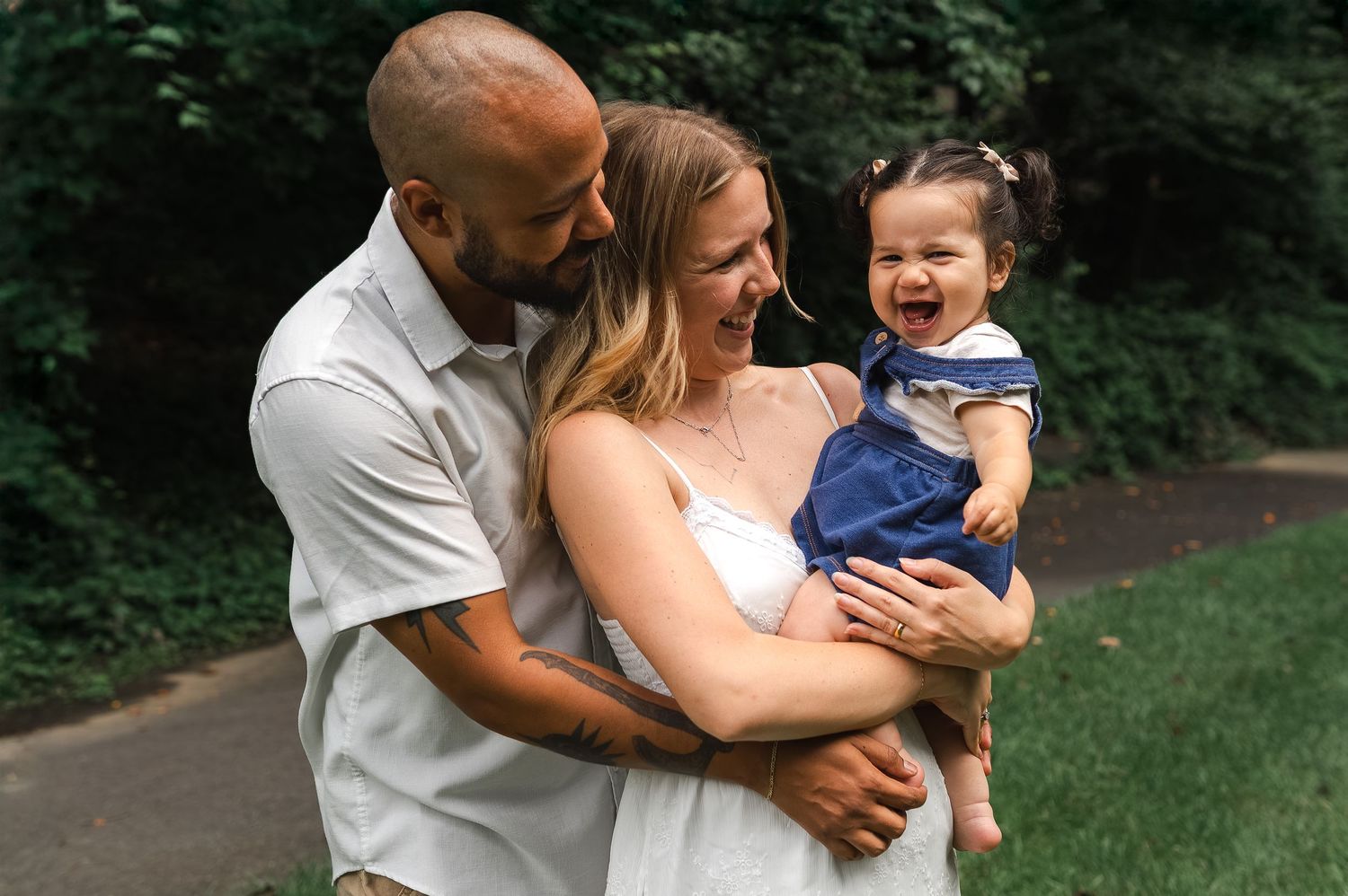 A loving family shares a joyful moment together outdoors on a pathway surrounded by green foliage.