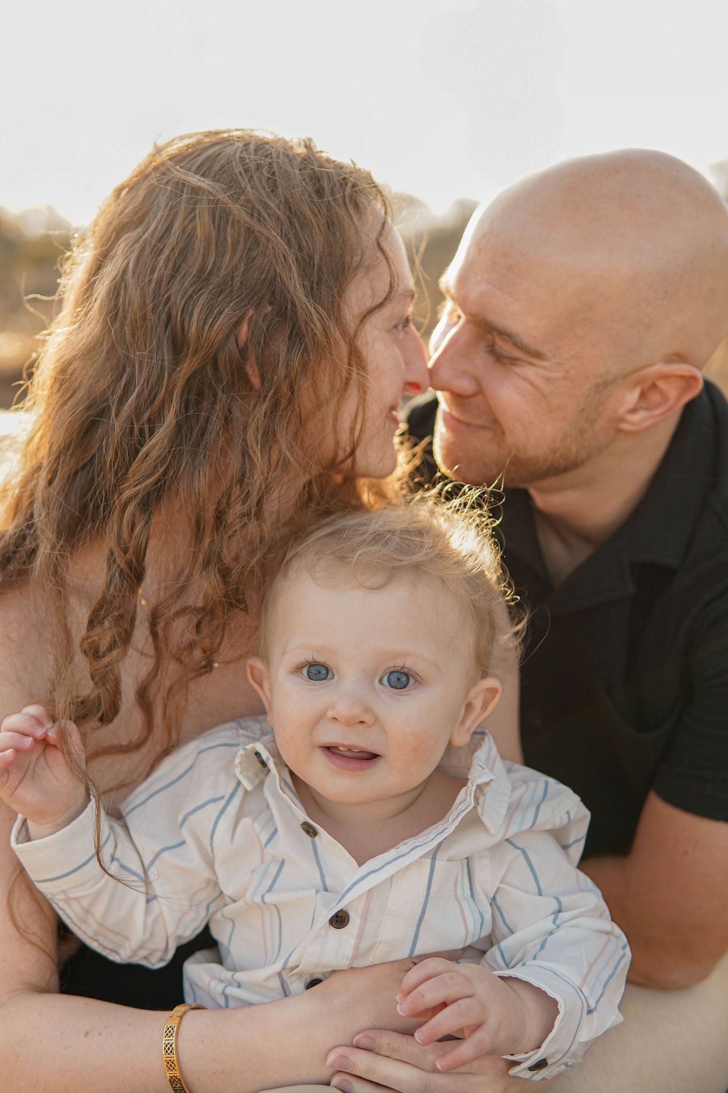 Sweet outdoor family portraits showing tender moments between parents and baby at sunset with natural lighting.
