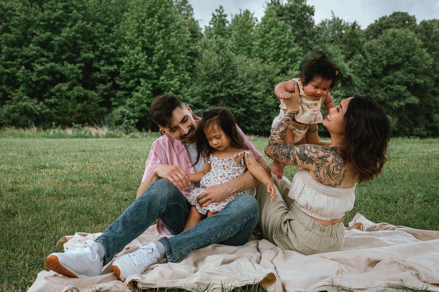 Family lounging together on a blanket in a park setting during a casual outdoor photoshoot.