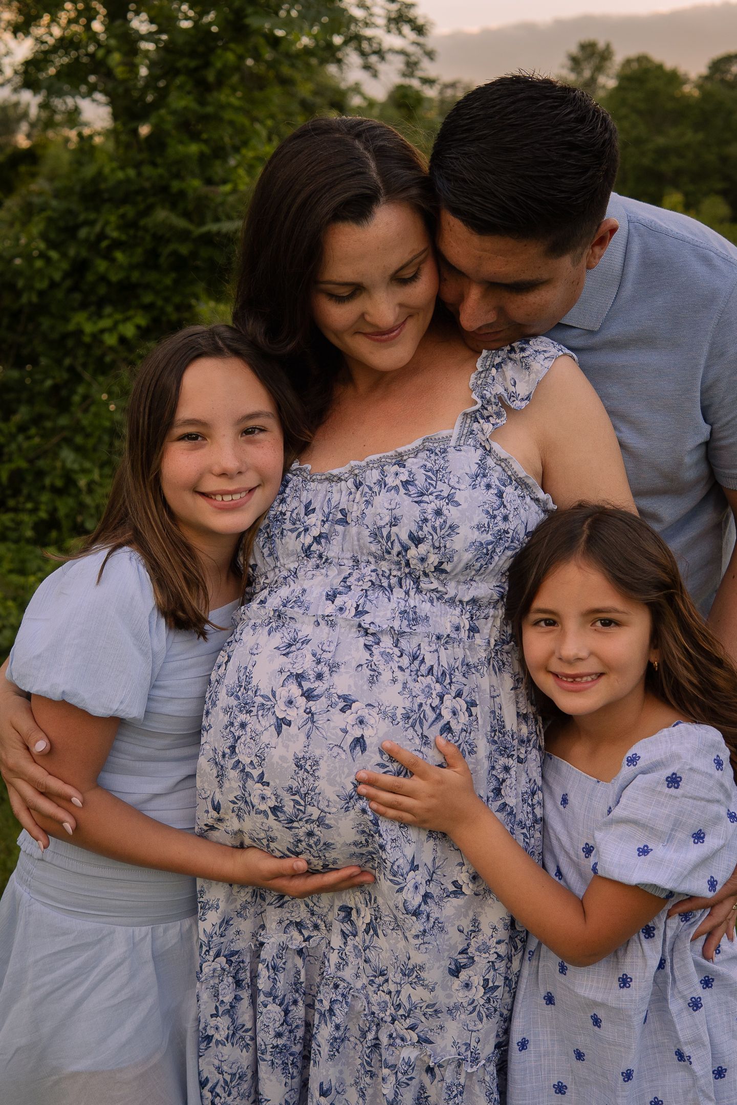 A growing family poses together outdoors as they celebrate an upcoming addition to their household during golden hour.