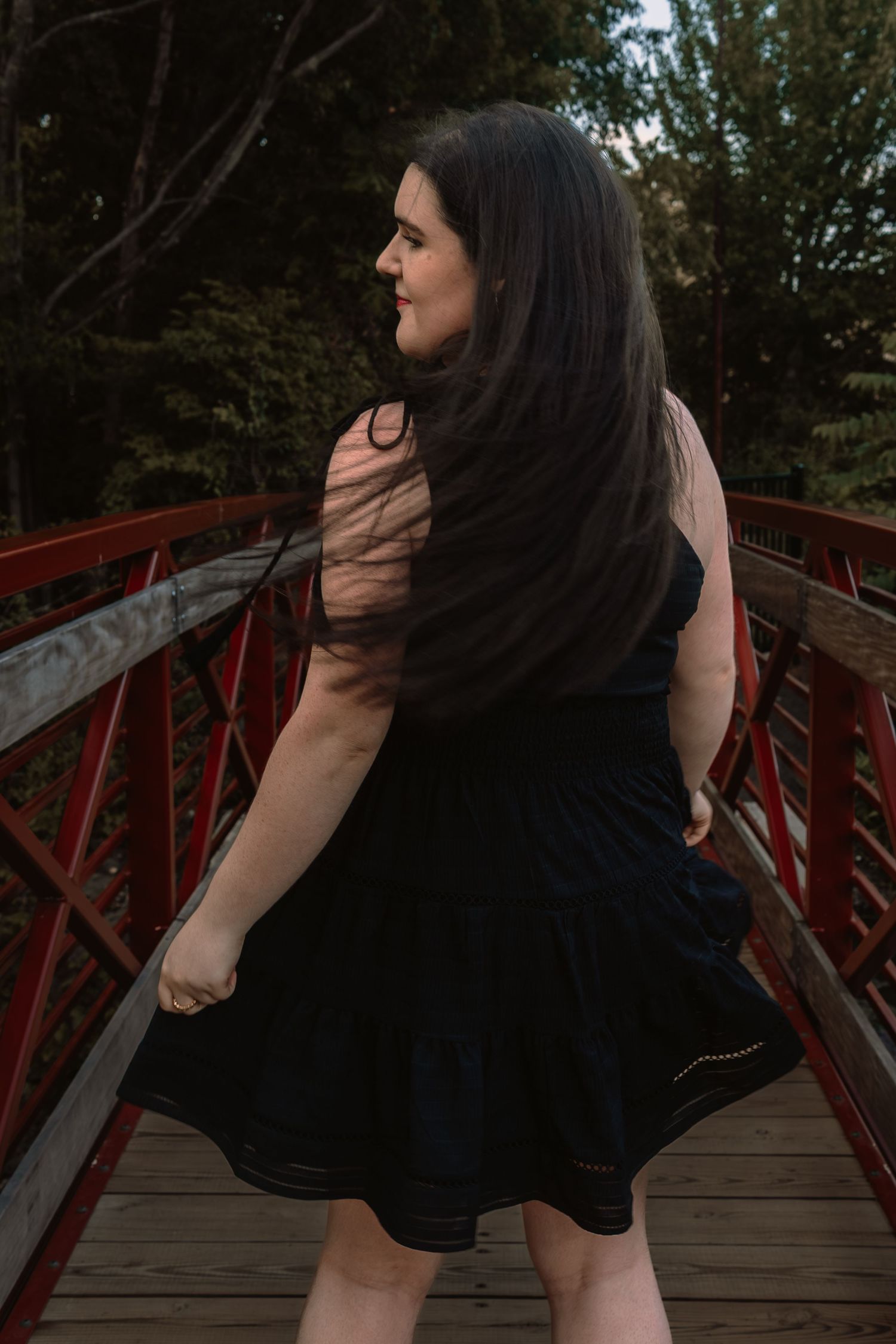 A person in a black dress poses on a red wooden bridge in a series of artistic outdoor photographs.