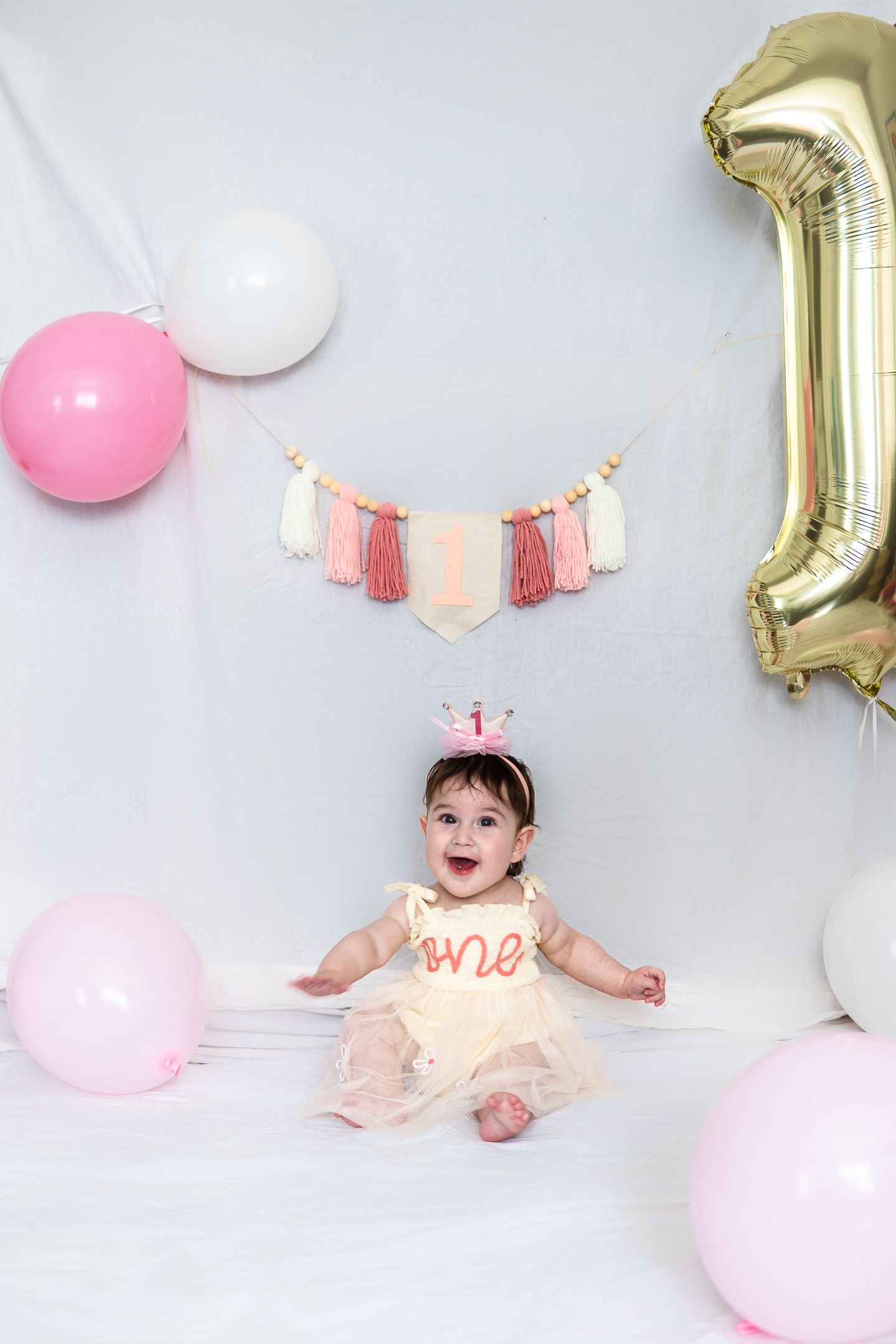 Birthday photo with pink and white balloons, tassel banner, and gold number one balloon.