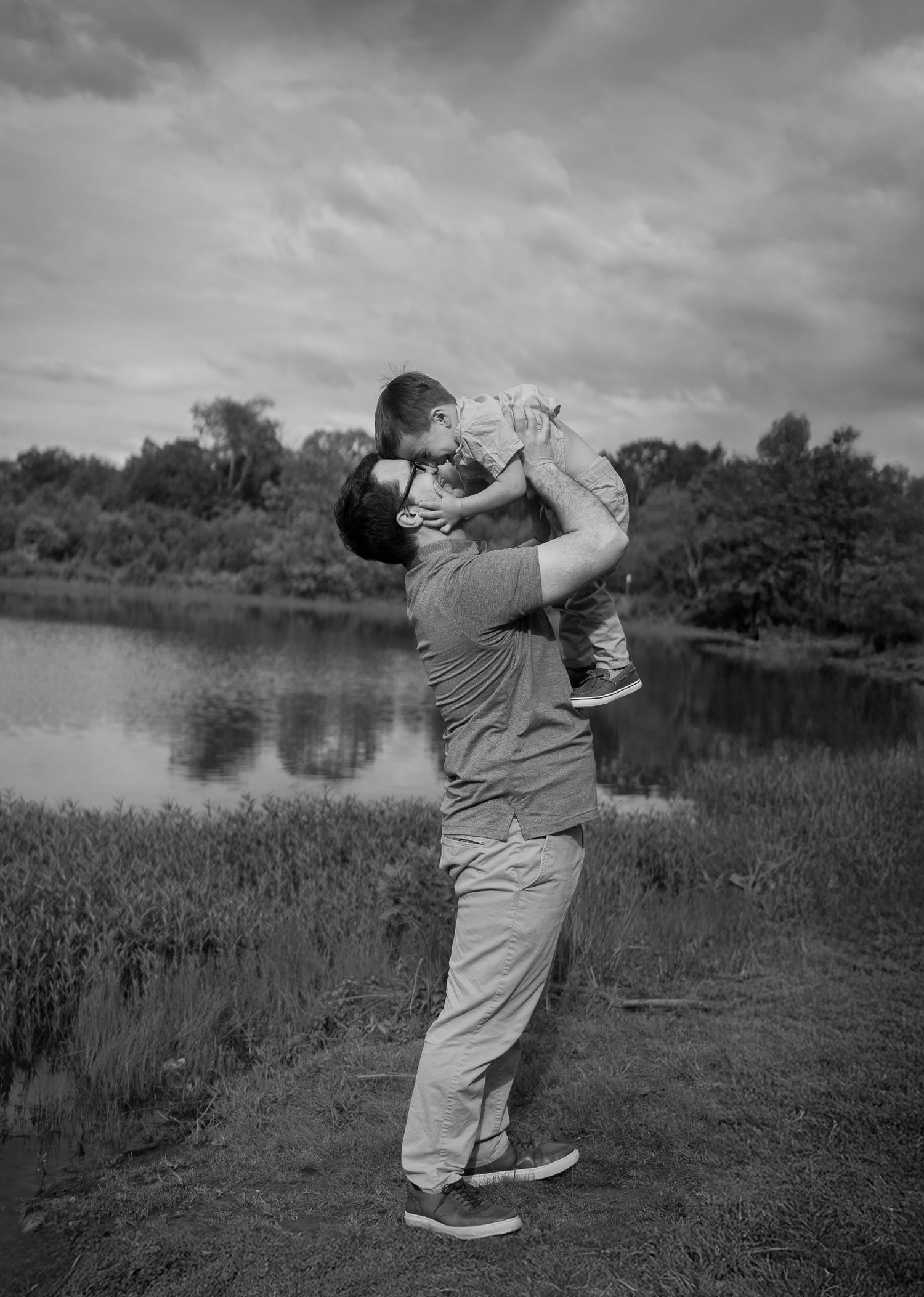 Black and white photo showing a joyful moment between adult and child by a tranquil lake.