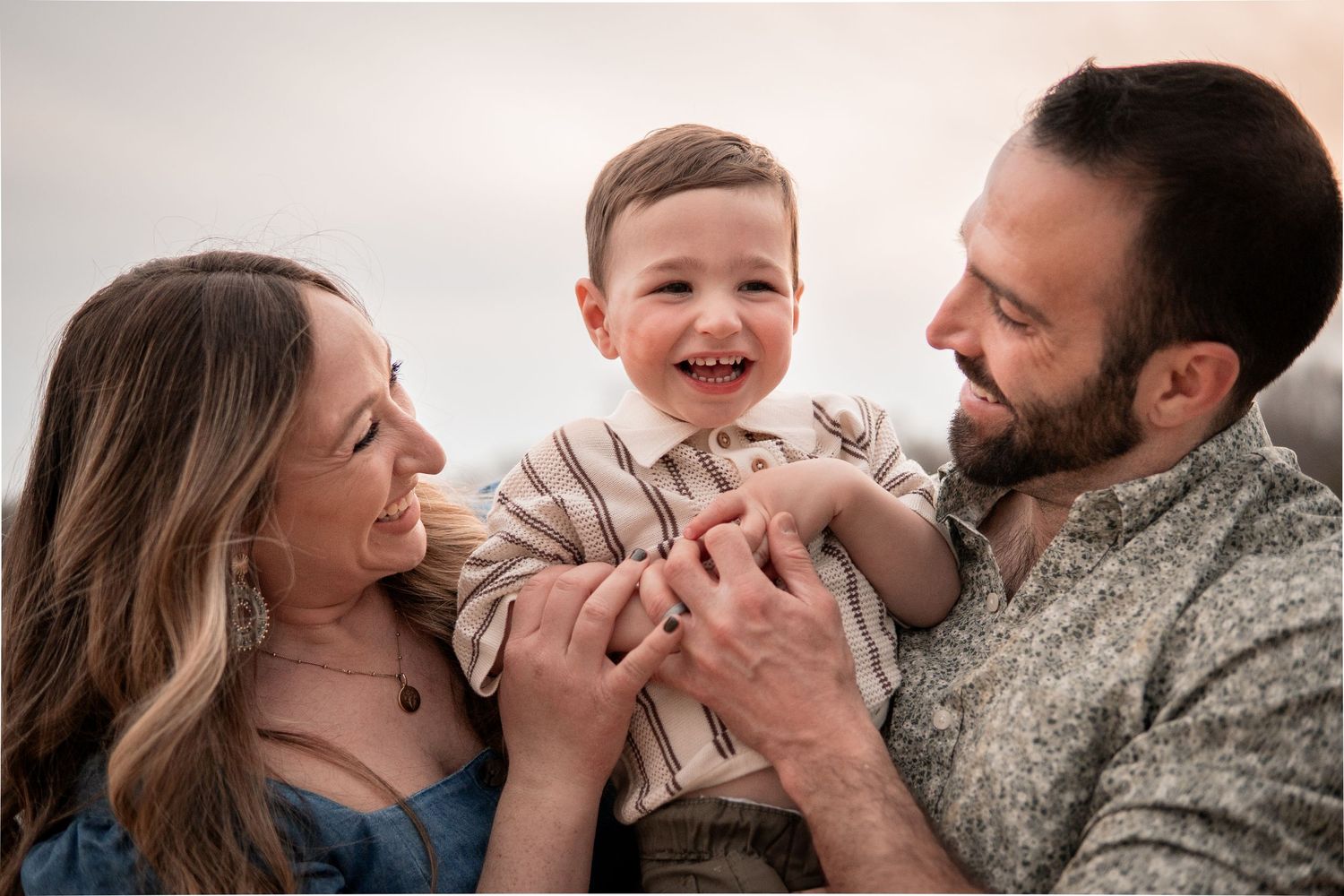 Three family members share a joyful moment together as they laugh and embrace while dressed in casual clothing.