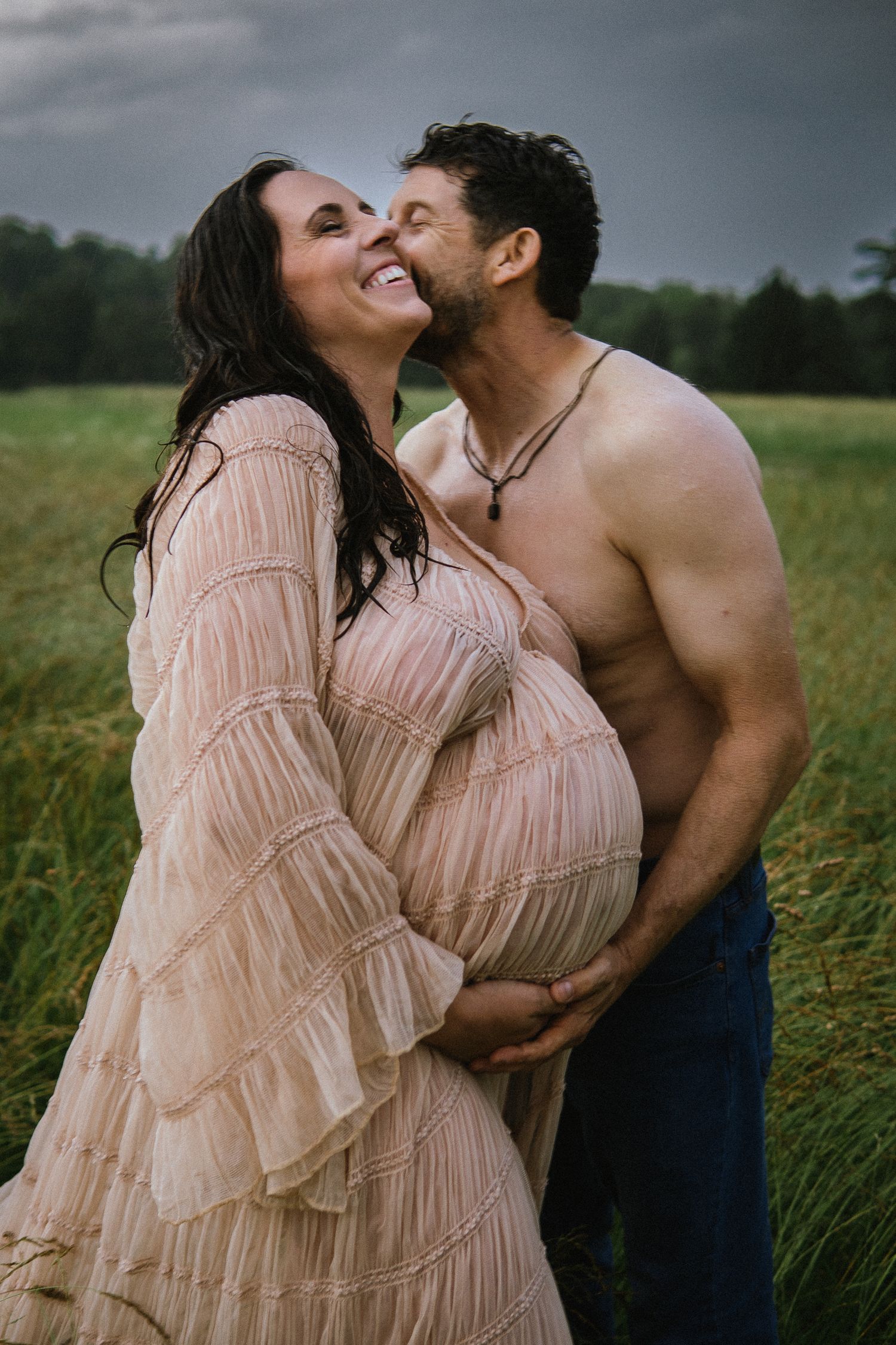 A joyful maternity photo of a couple laughing together in a green field.