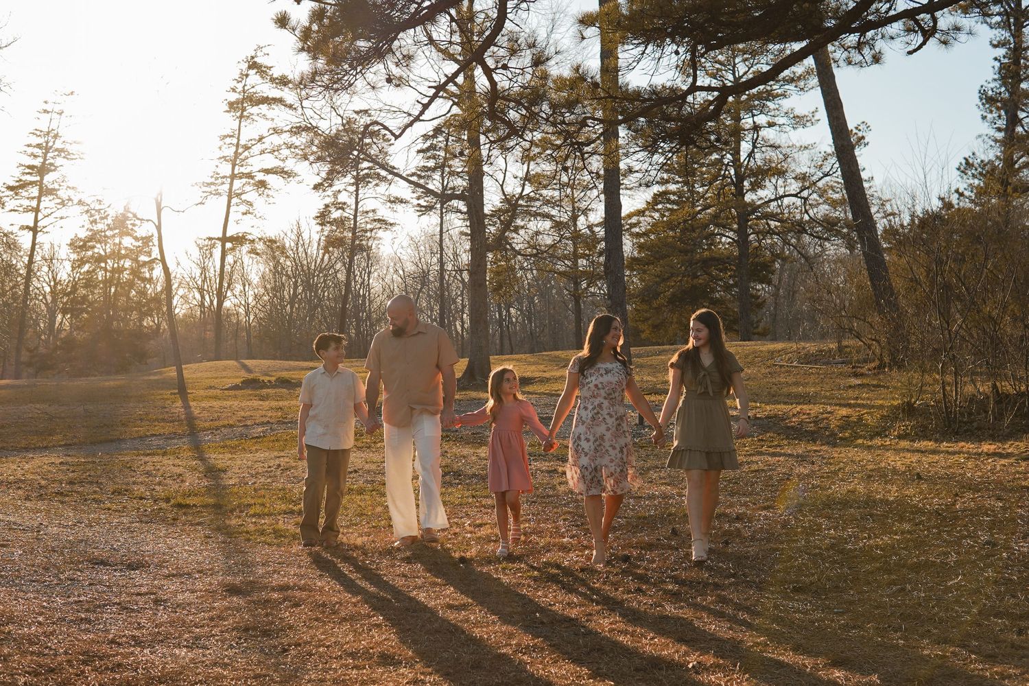 Family walking together through pine trees during golden hour sunset.