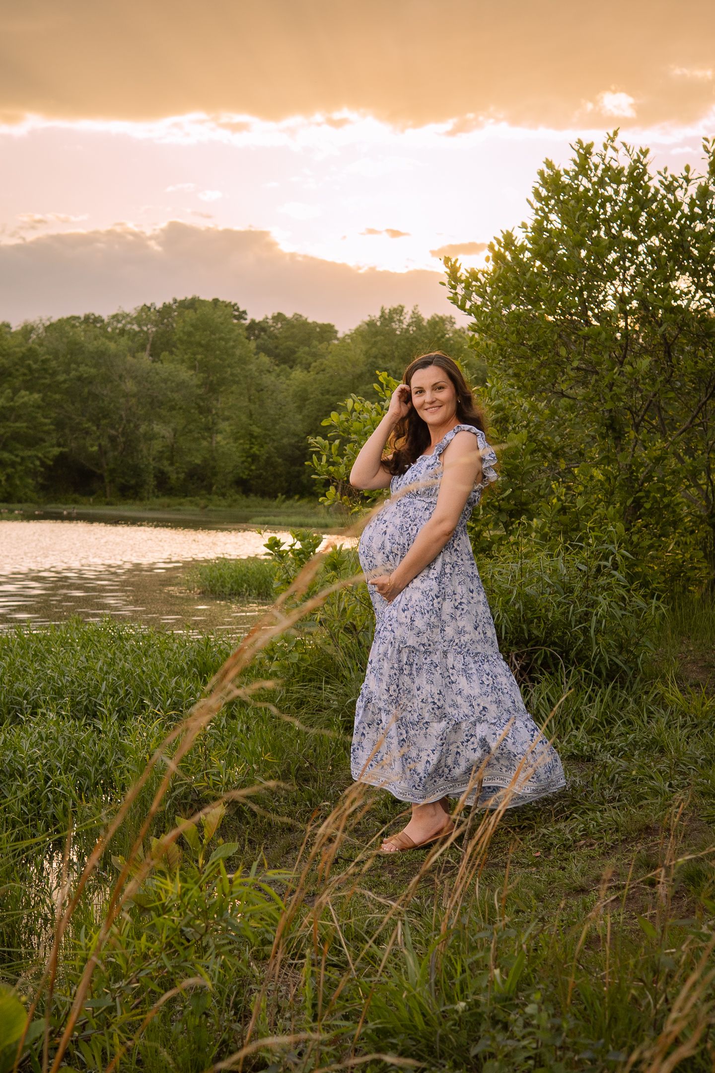 A floral maxi dress worn near a serene lake at sunset with tall grasses in the foreground.