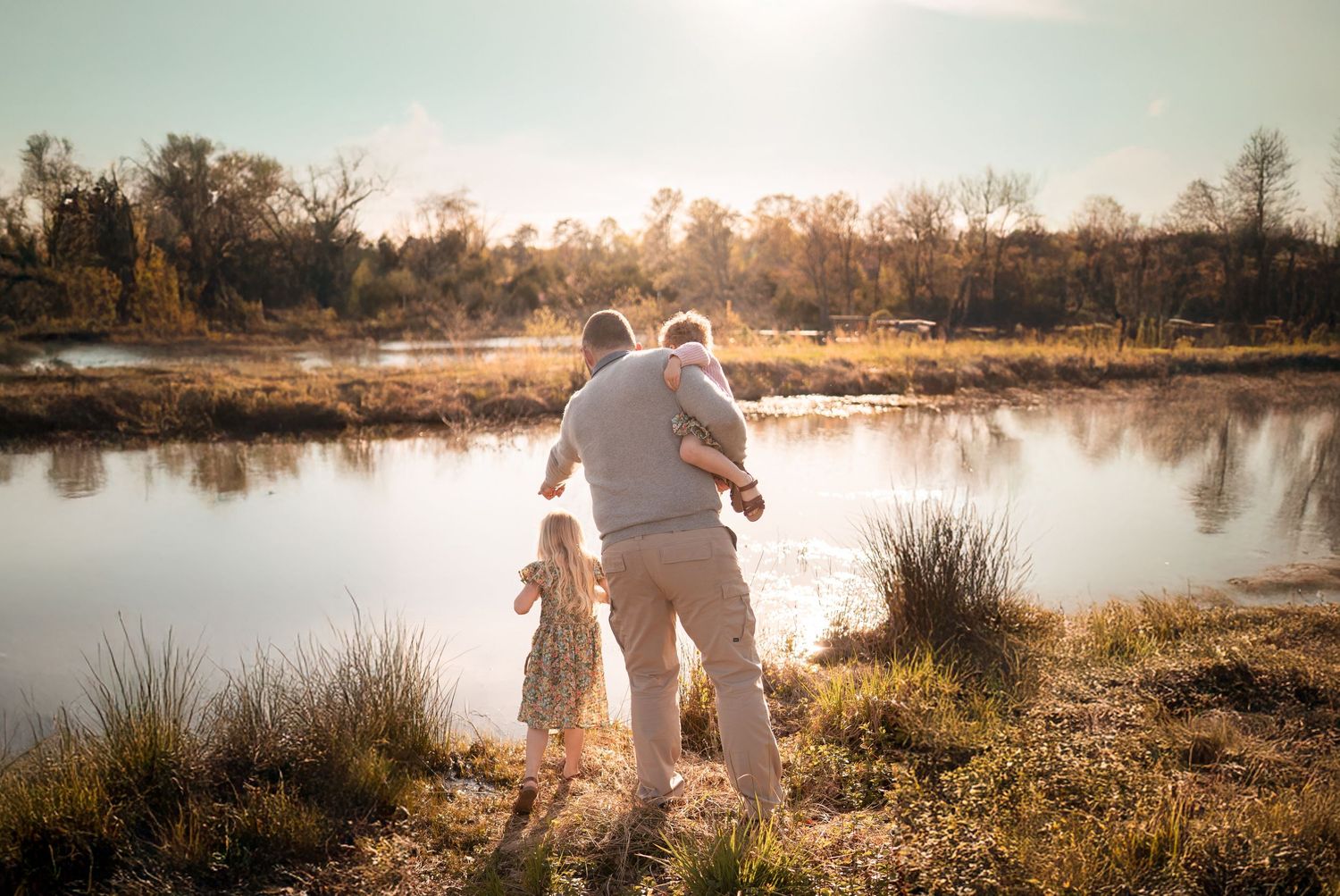 Two figures stand together gazing at a serene pond during golden hour with trees silhouetted against the setting sun in Haymarket, Virginia.
