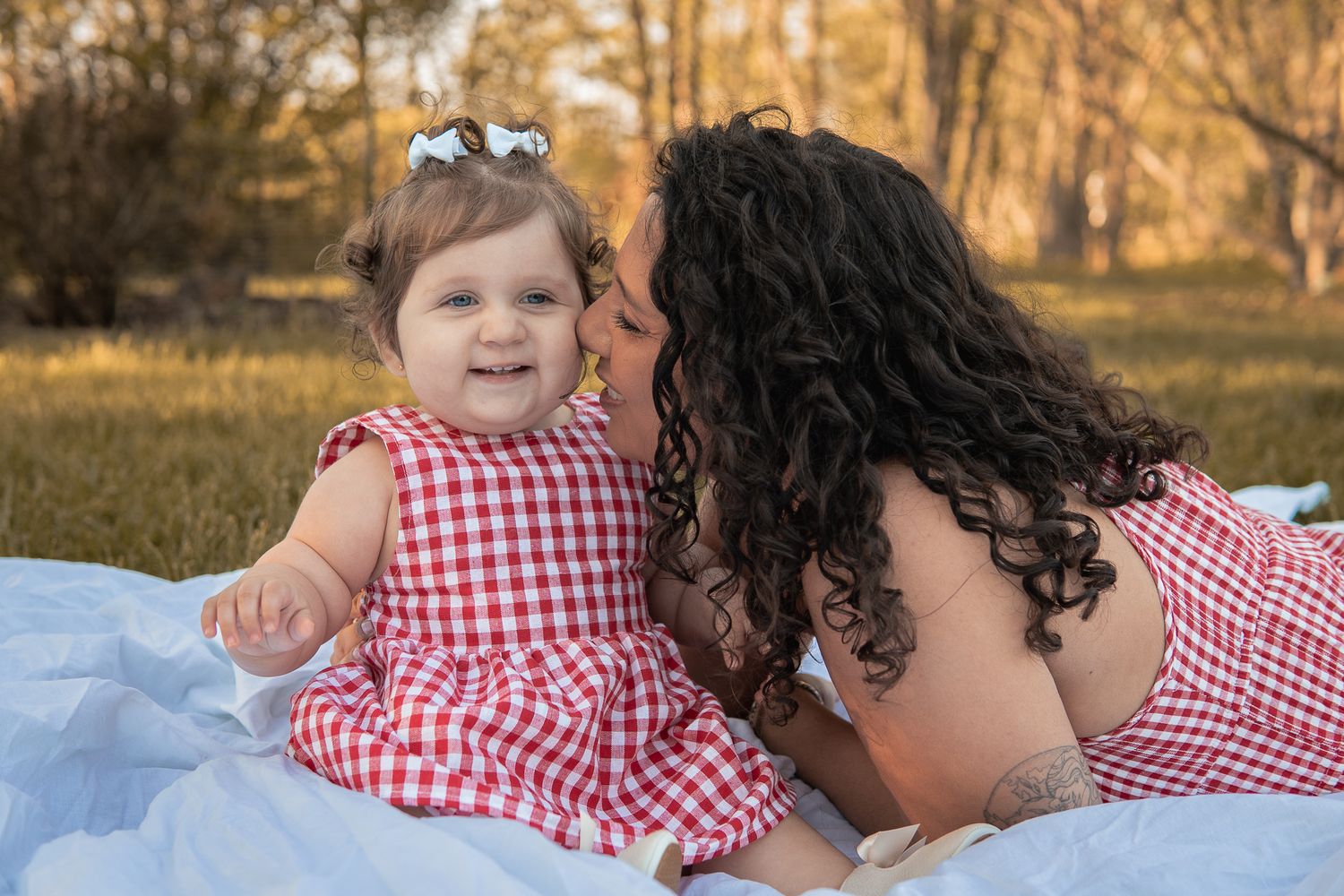 A sweet moment shared on a picnic blanket with matching red gingham dresses in a sunlit autumn setting.