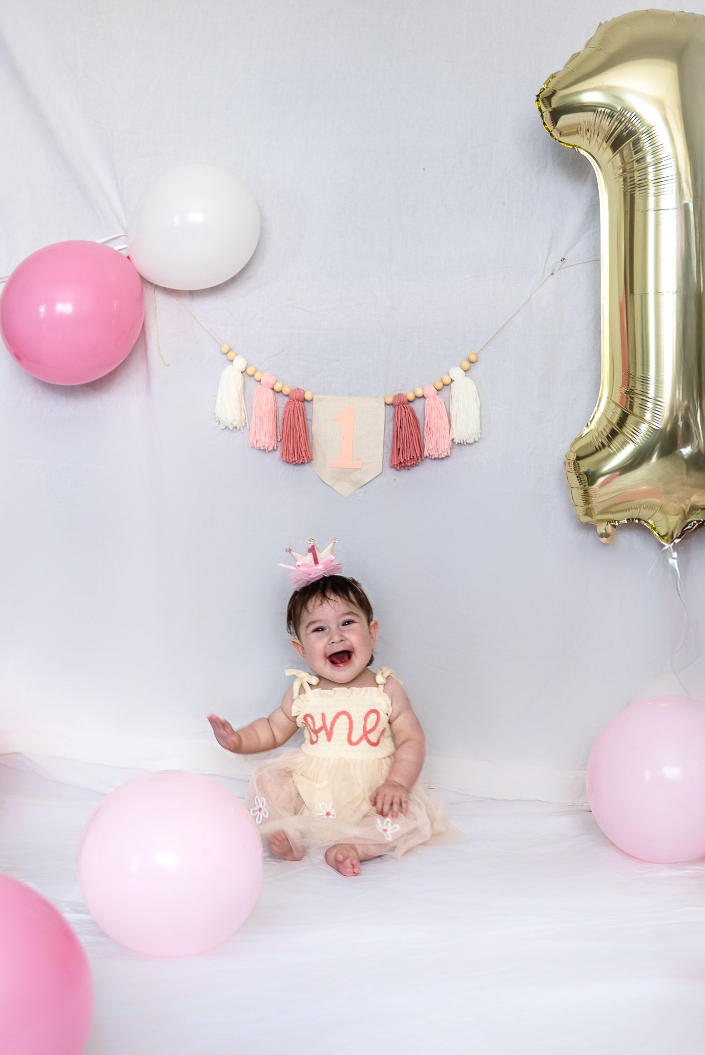 Birthday party setup with pink and white balloons, tassels, and a gold number 1 balloon.