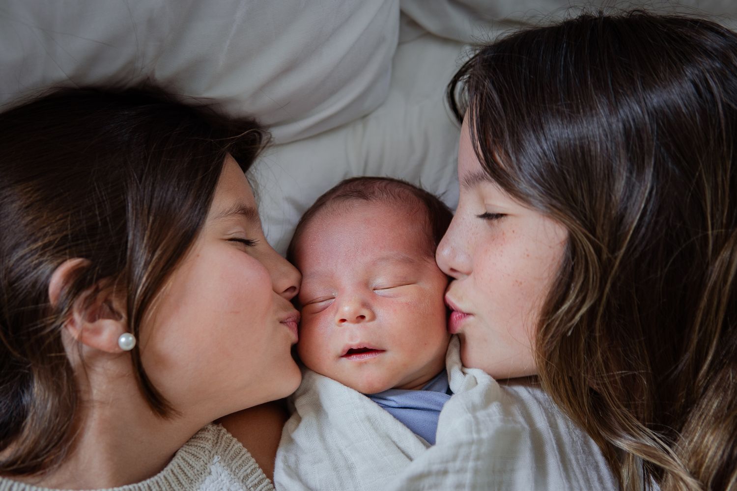 Tender family moment showing siblings snuggling together on white bedding.