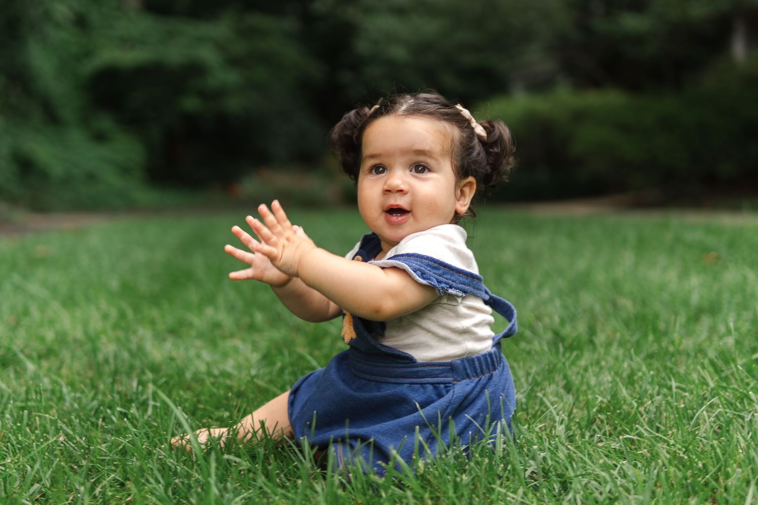 Small child in blue shirt plays and rolls on lush green grass outdoors on sunny day.