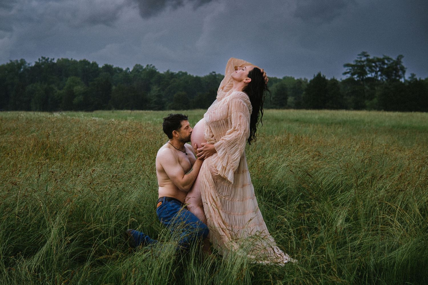 A loving couple shares tender moments in a field of grass against a dramatic stormy sky.