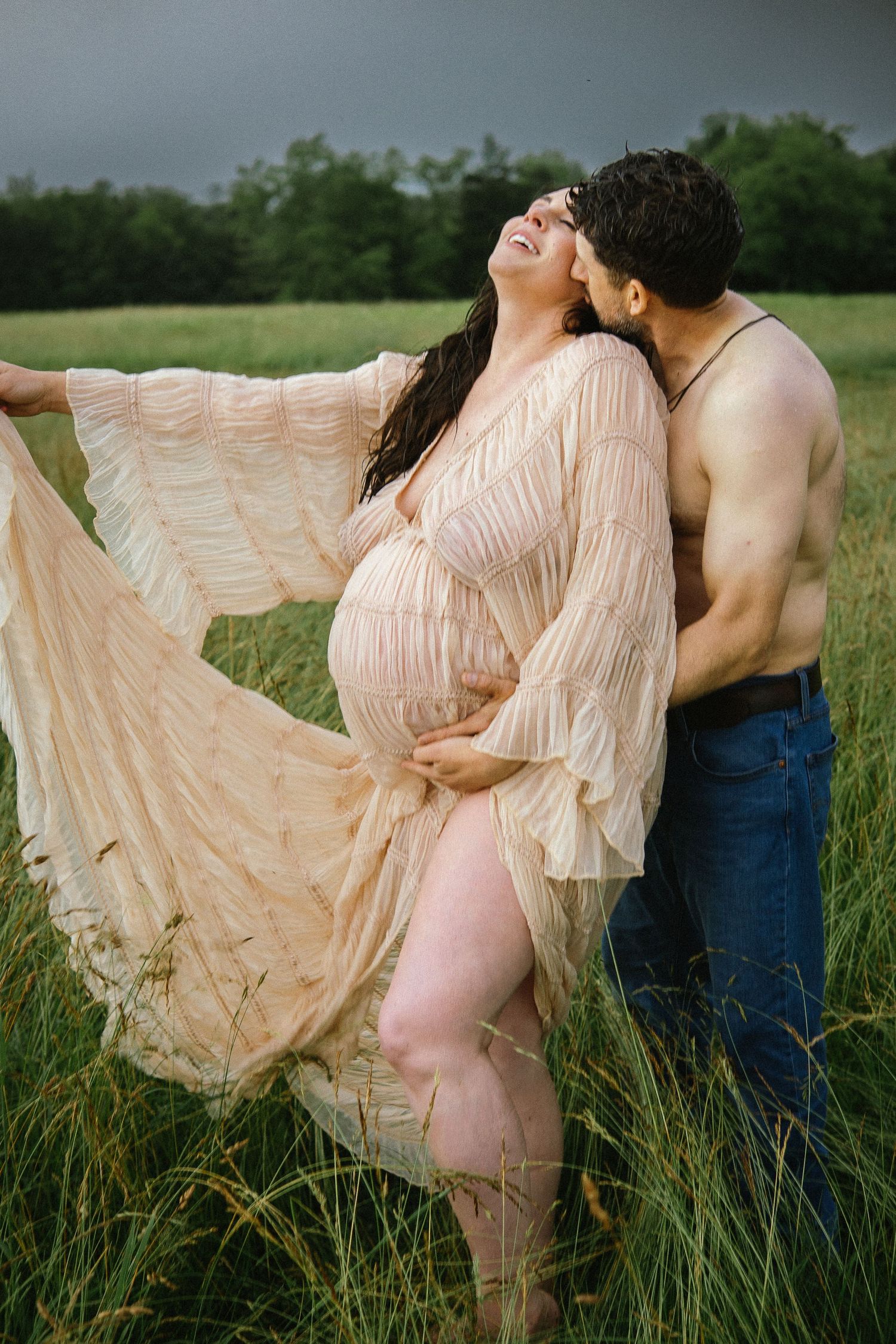 A couple embraces in a field, with the woman wearing a flowing peach dress against a moody sky.