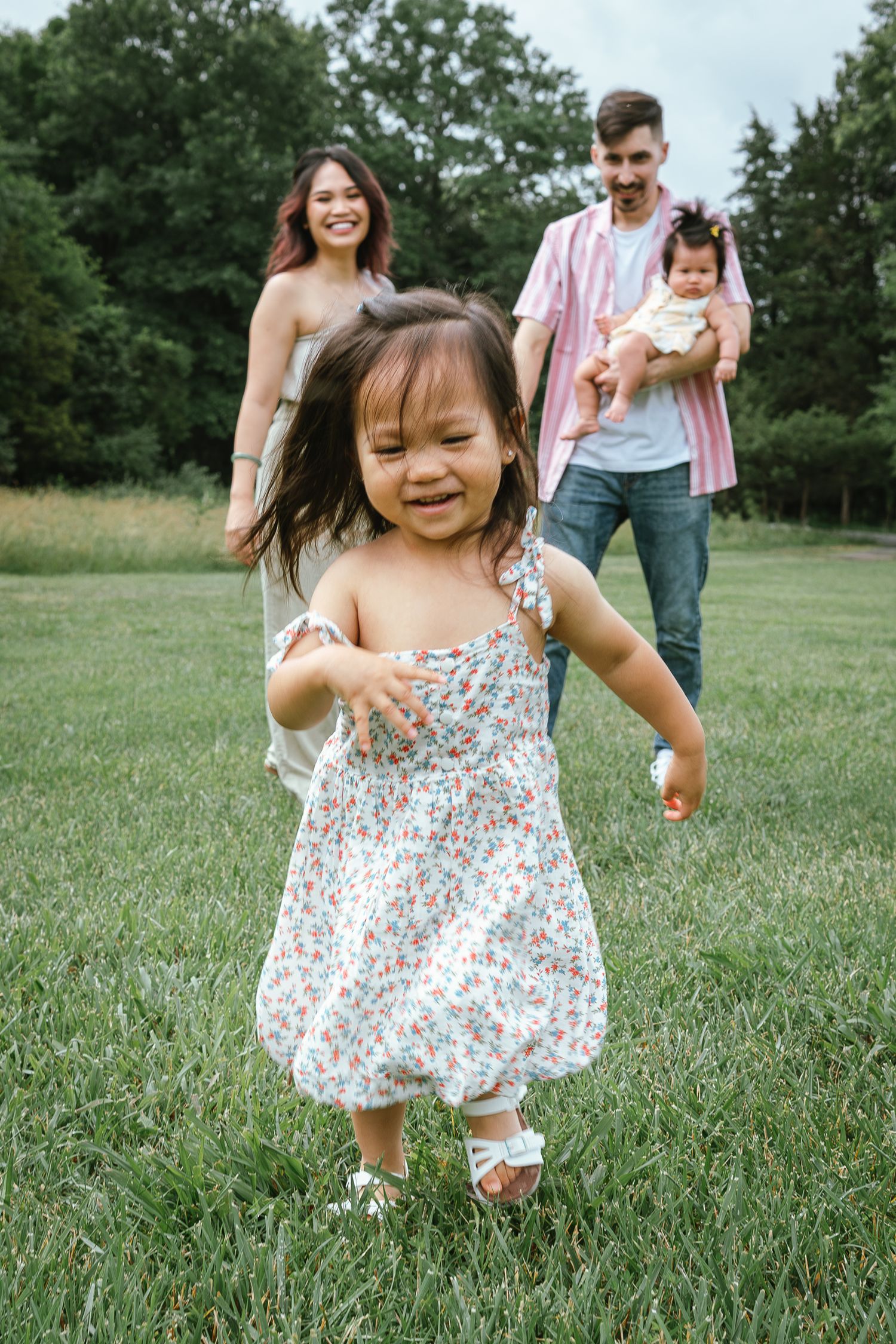 A small child in a floral dress runs happily through a green field during a summer photoshoot.