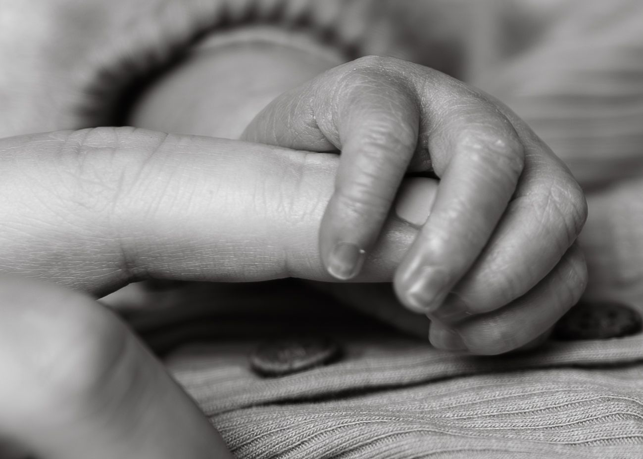 Black and white close-up photograph of hands gently resting on a textured surface.