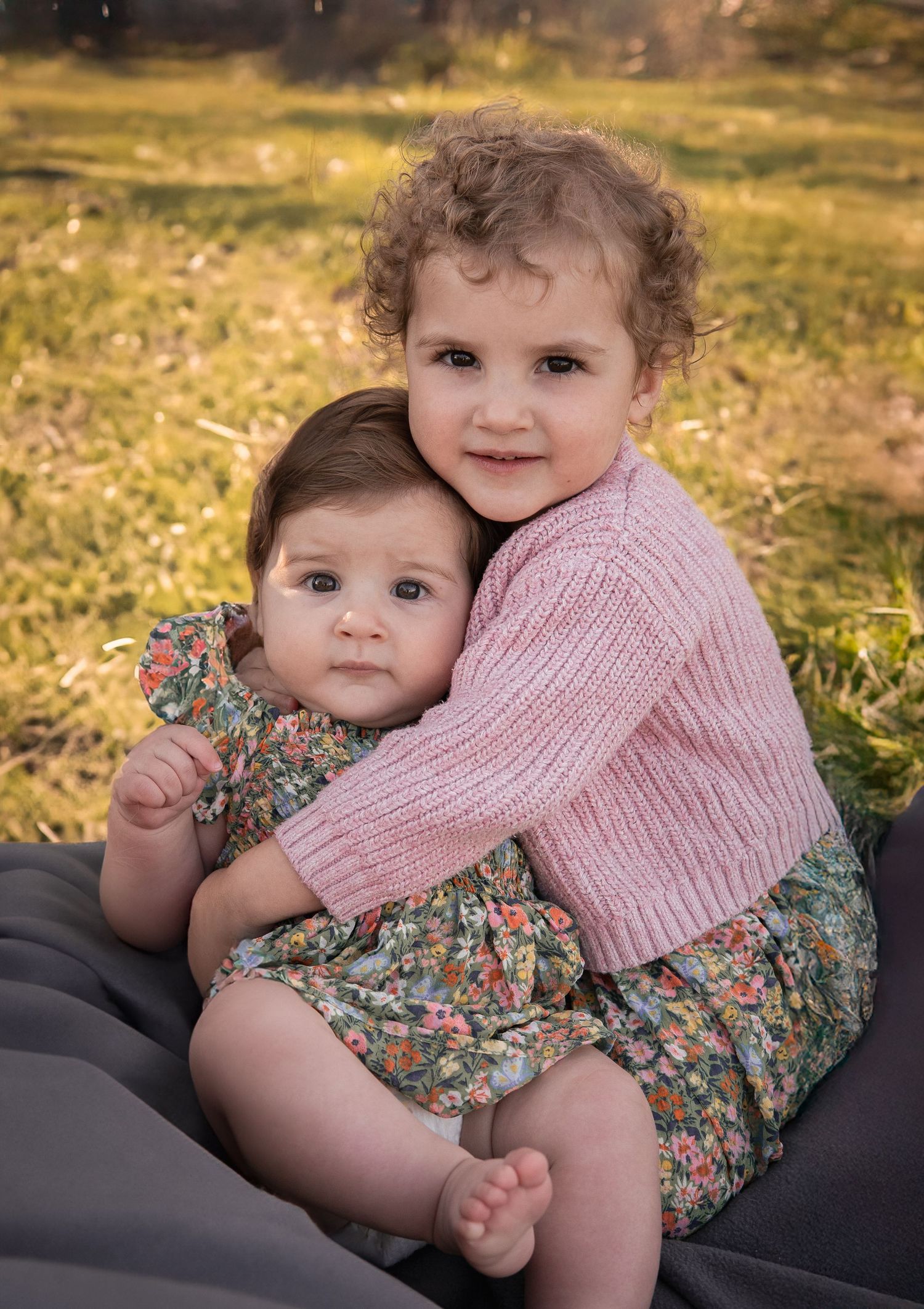 Two small children hugging while sitting outdoors in a sunlit autumn setting.
