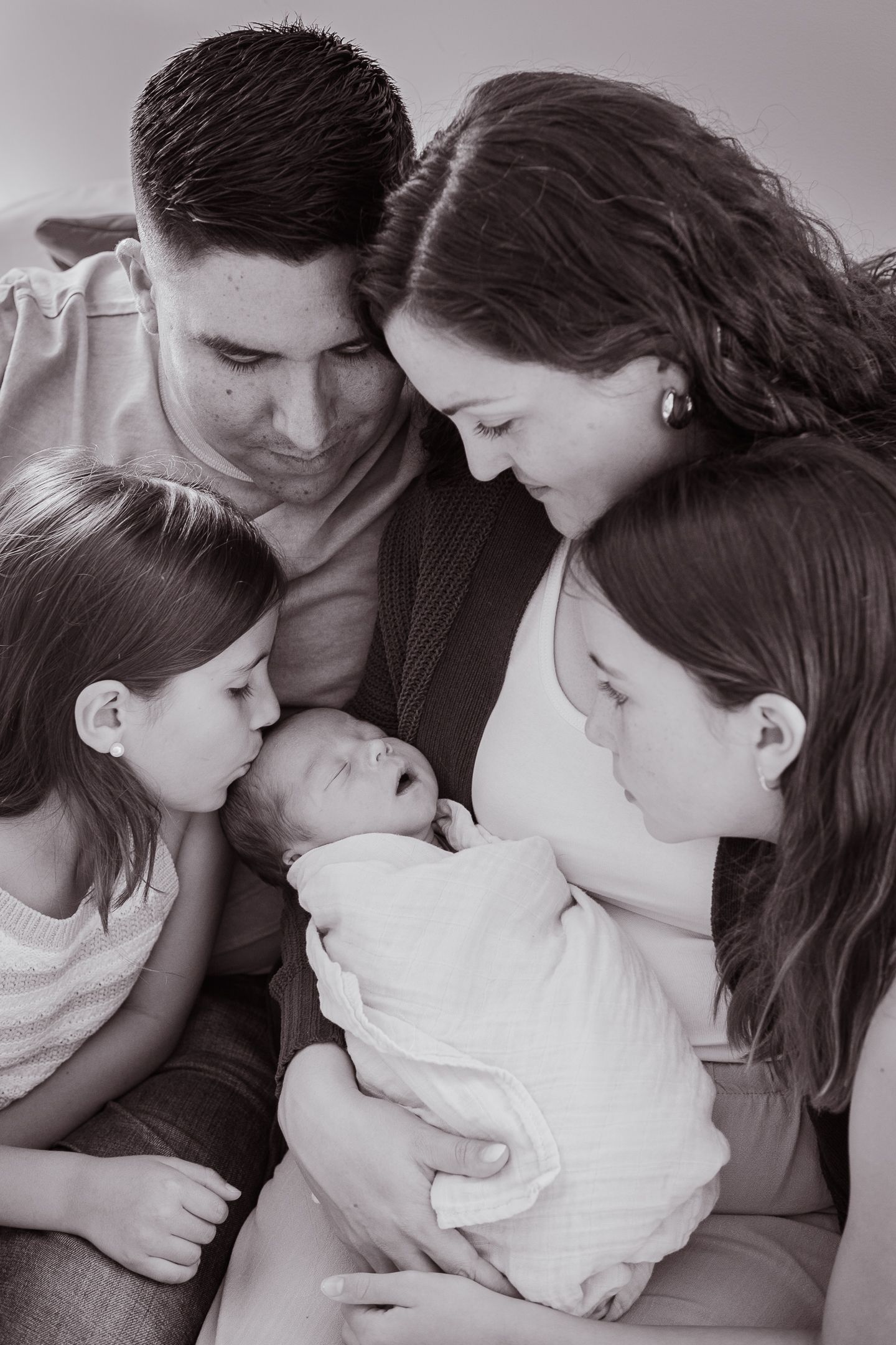 A family gathers close together to admire their newborn baby in a tender black and white portrait.