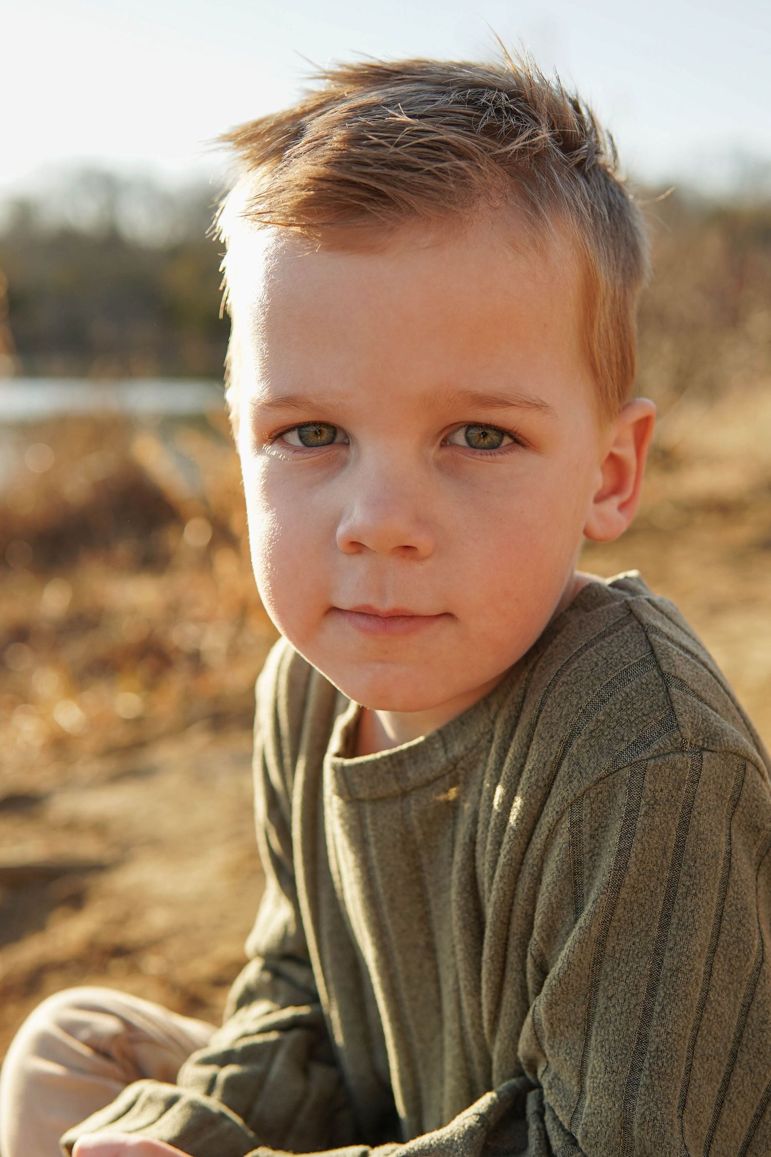 Close-up outdoor portrait of young child in olive green sweater during golden hour lighting.