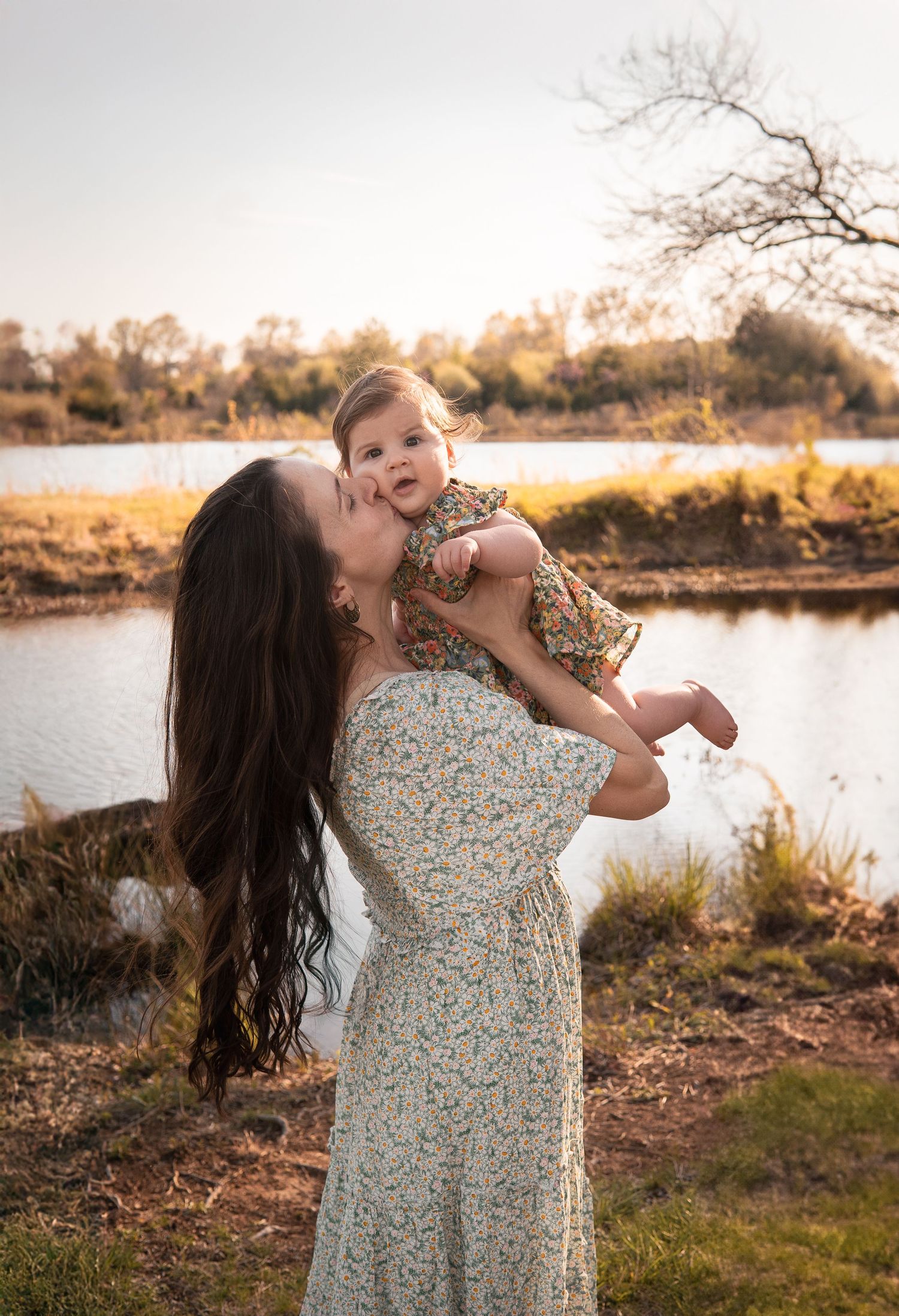 A heartwarming sunset portrait by a lake with golden light filtering through bare trees.