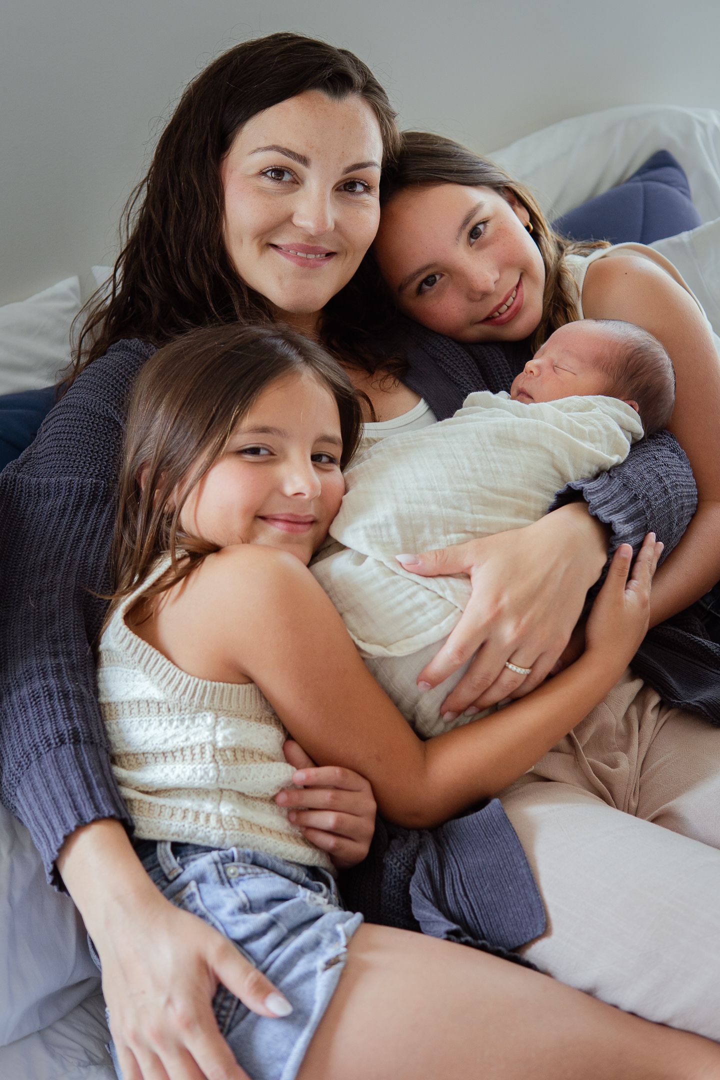 Family snuggling together on bed with newborn baby while sharing intimate bonding moment.