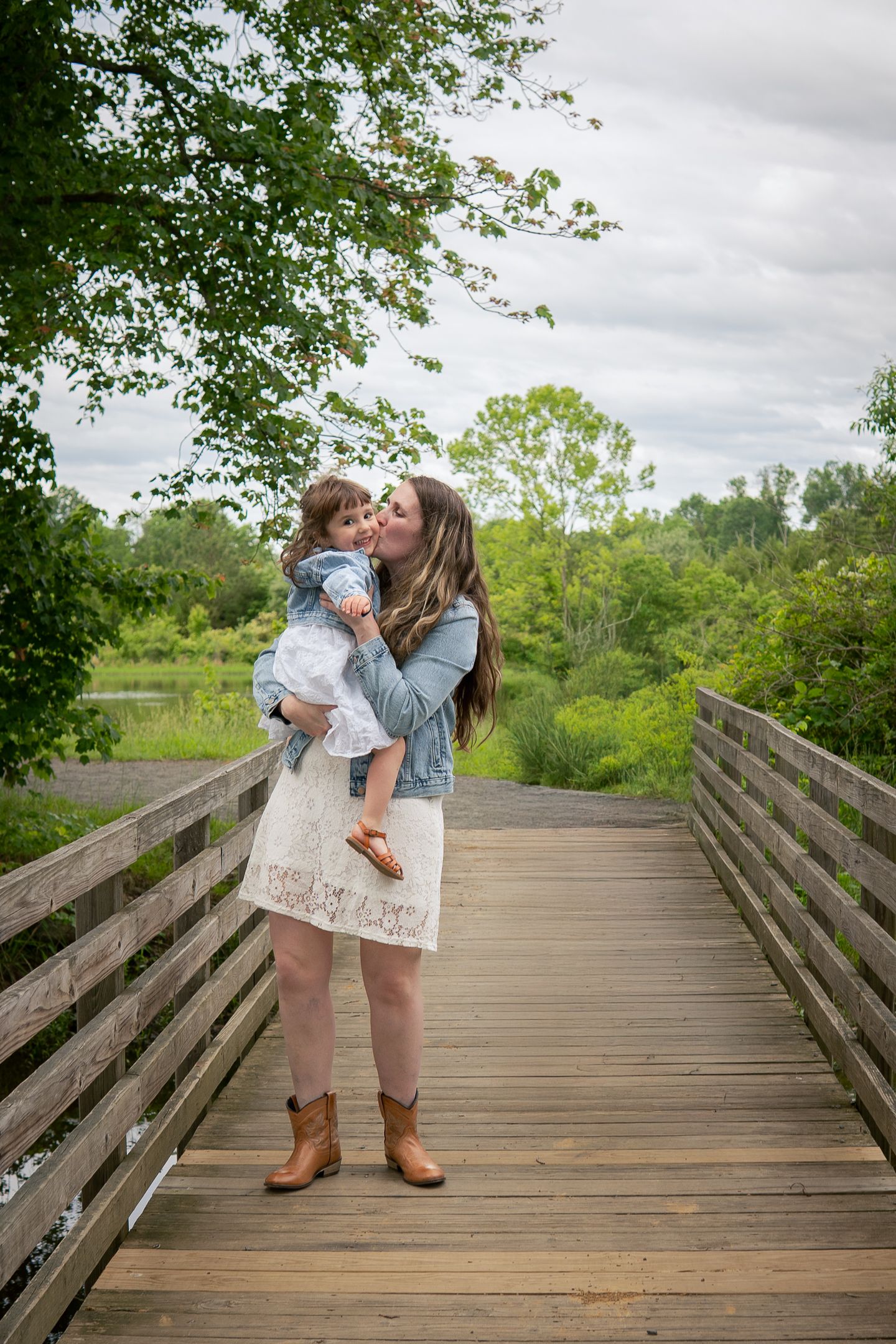 Candid family moments captured on a wooden boardwalk surrounded by lush green trees.
