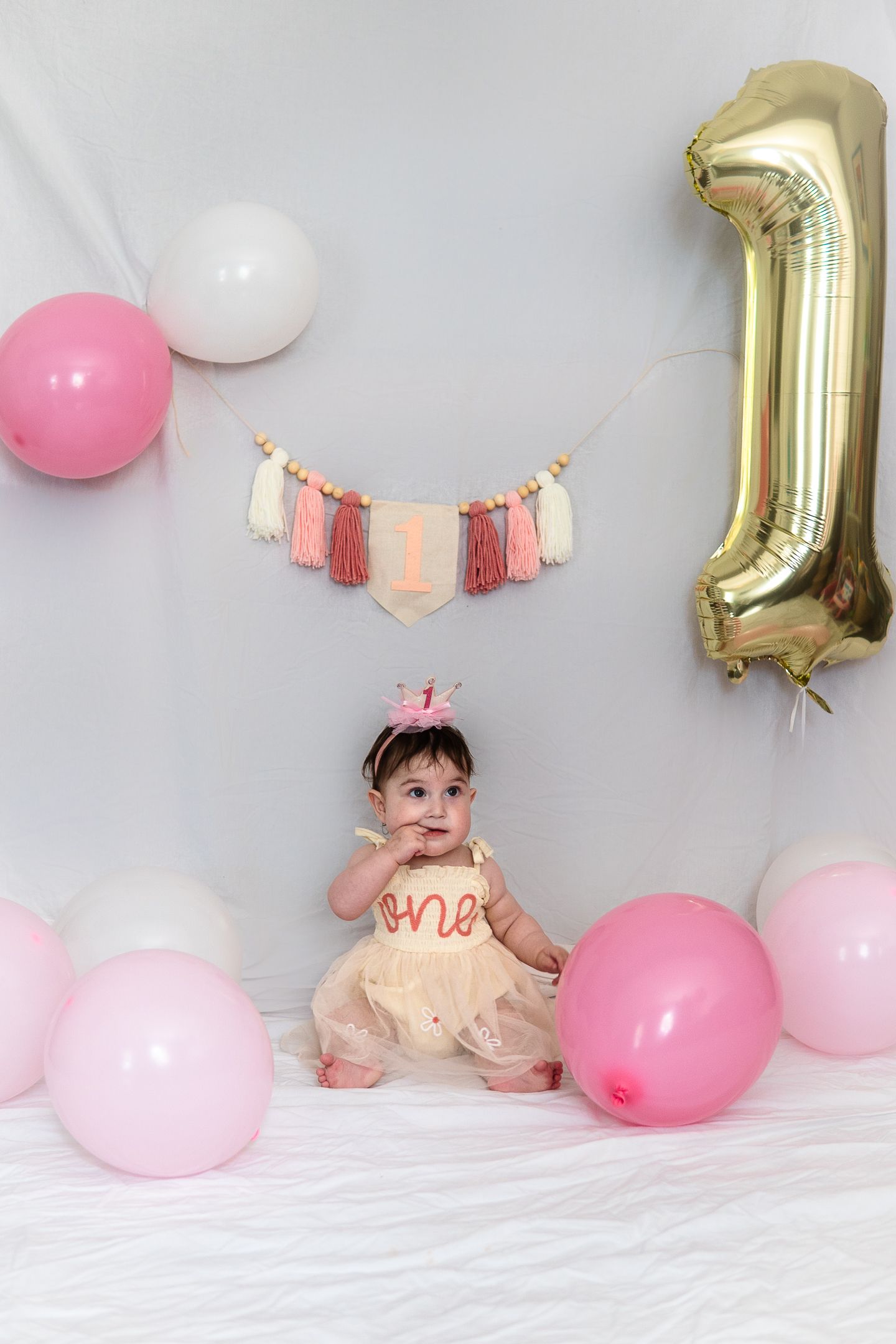 Birthday setup with gold number 1 balloon, pink and white balloons, and tassel garland decoration.
