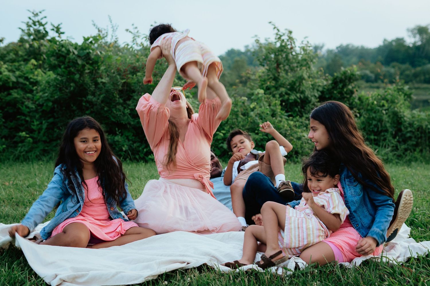 Family group having fun together while sitting on blanket for outdoor picnic.