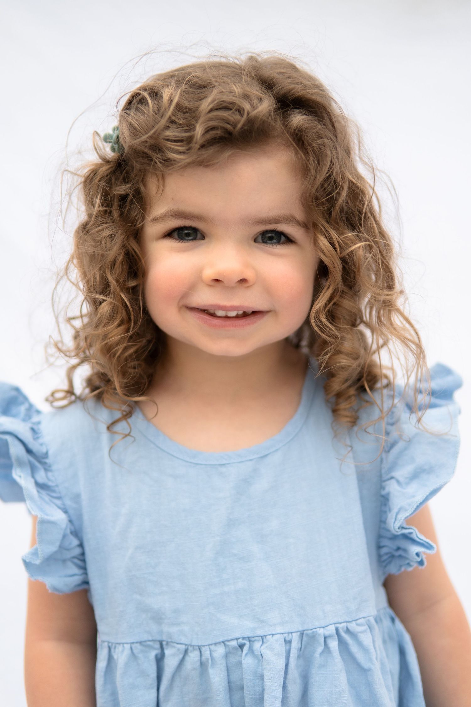 Sweet portrait series of a child with curly hair wearing a light blue dress against a white background.