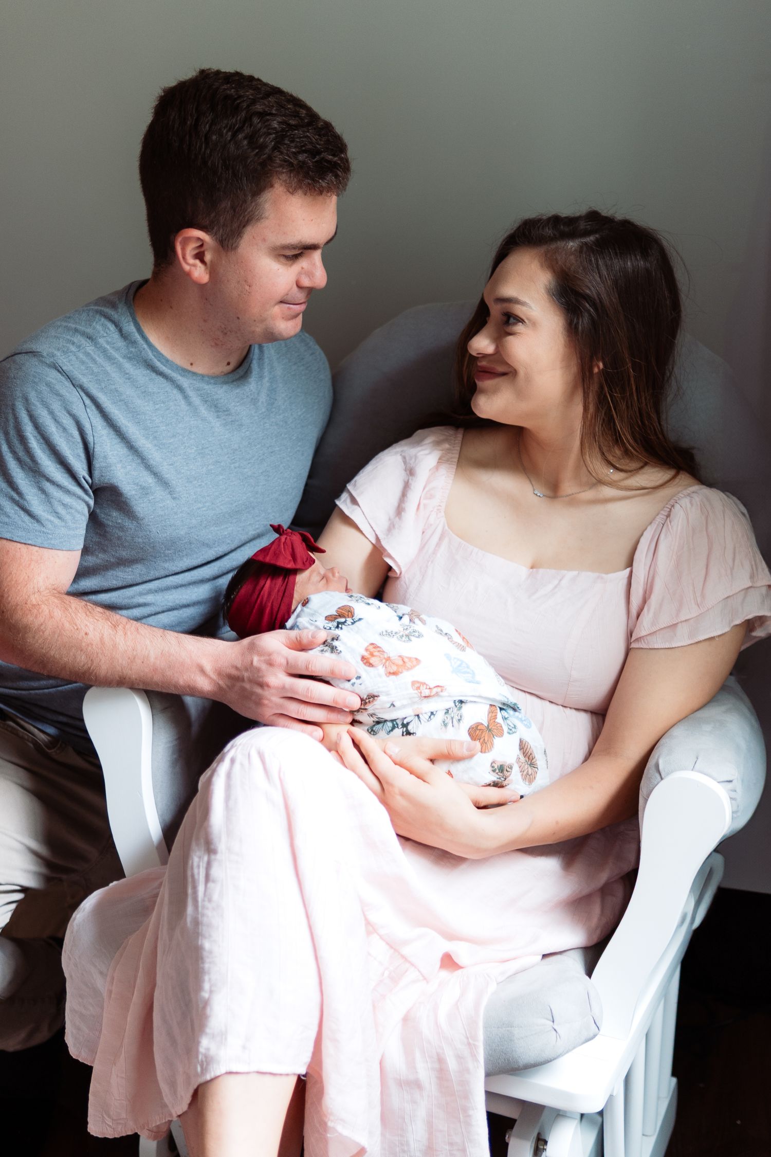 A tender moment between new parents sitting together while holding their swaddled newborn.