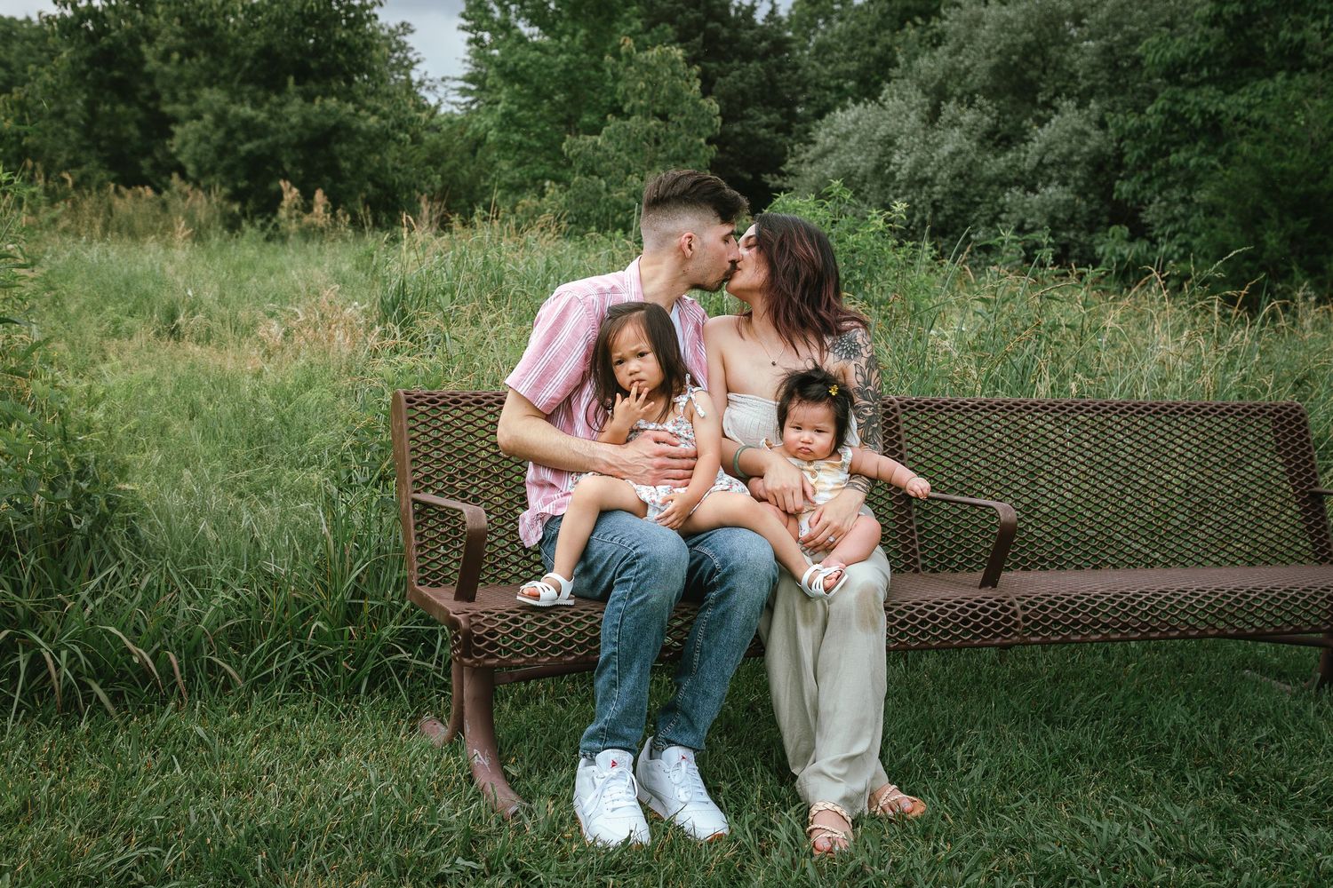 Relaxed family photo session on a park bench surrounded by lush greenery.