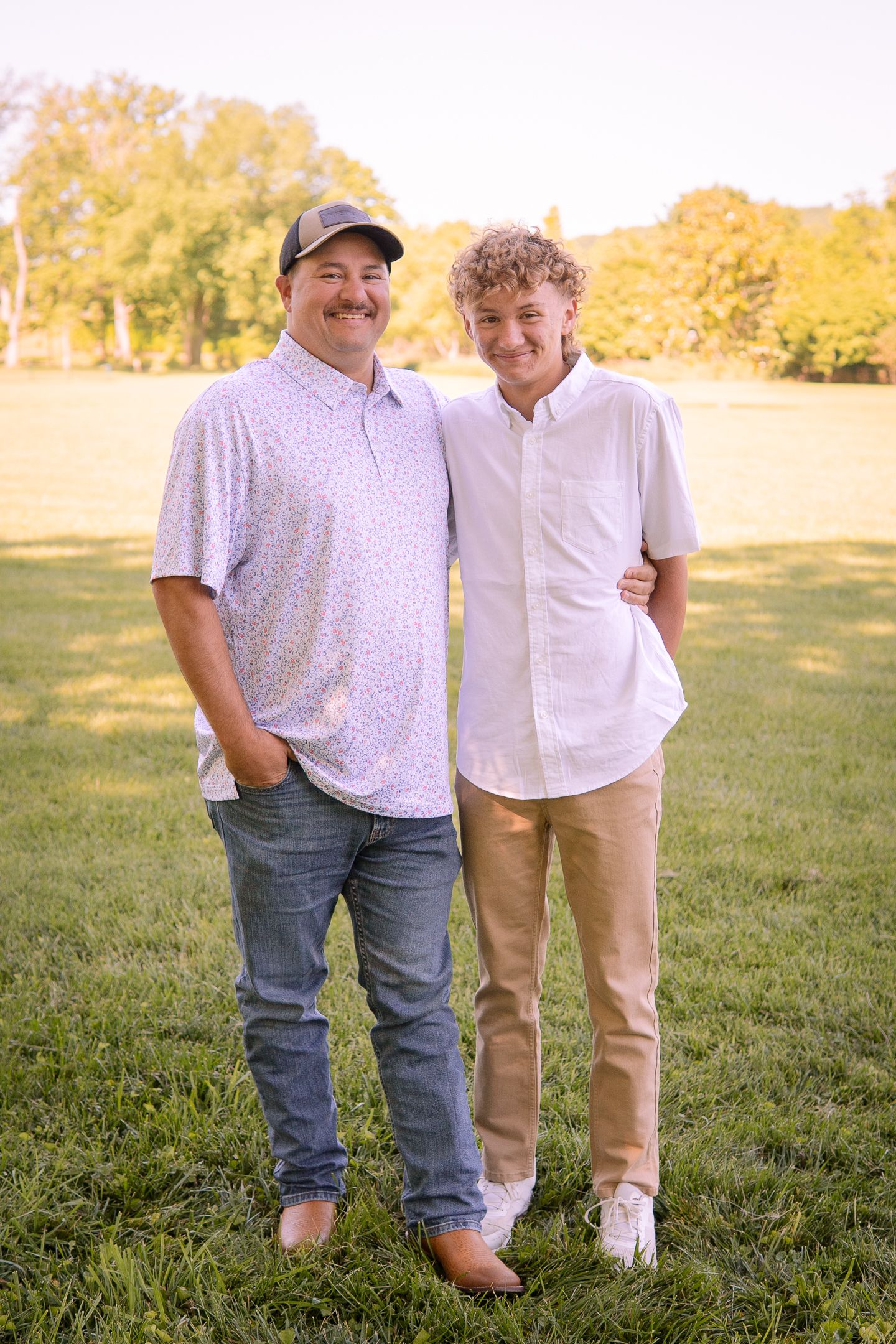 Two people standing together on grass with trees in background during golden hour.