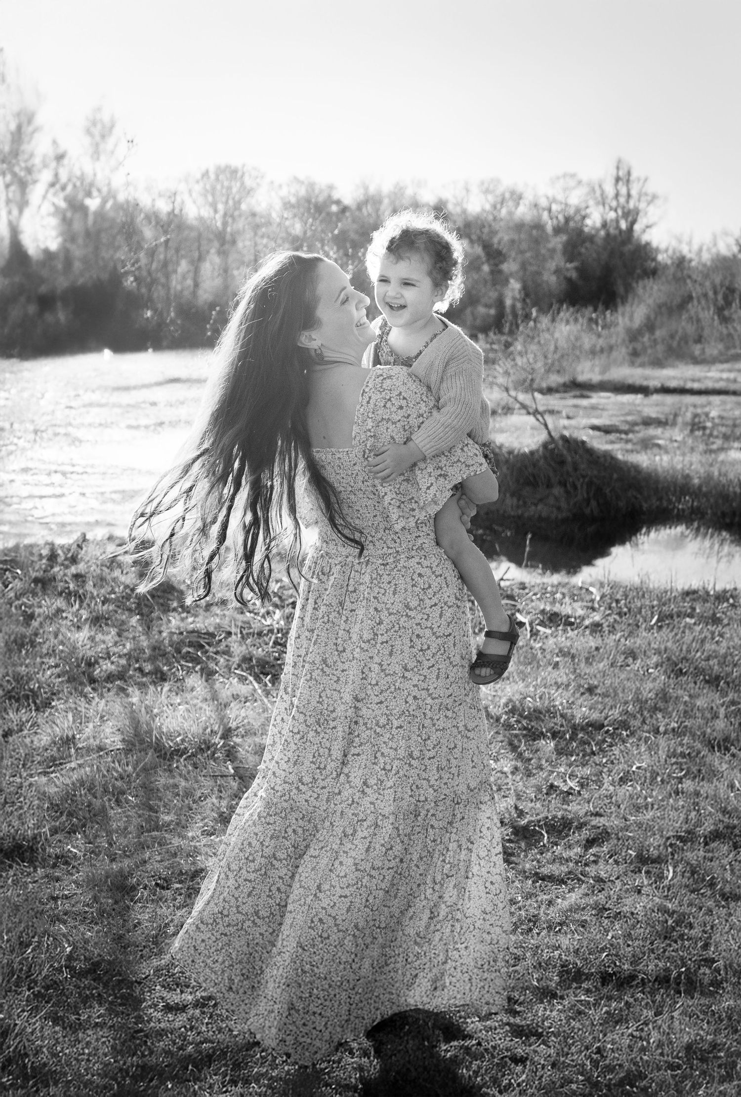 A tender moment captured in black and white showing a parent and child embracing outdoors in flowing floral dress at sunset in Haymarket, Vi
