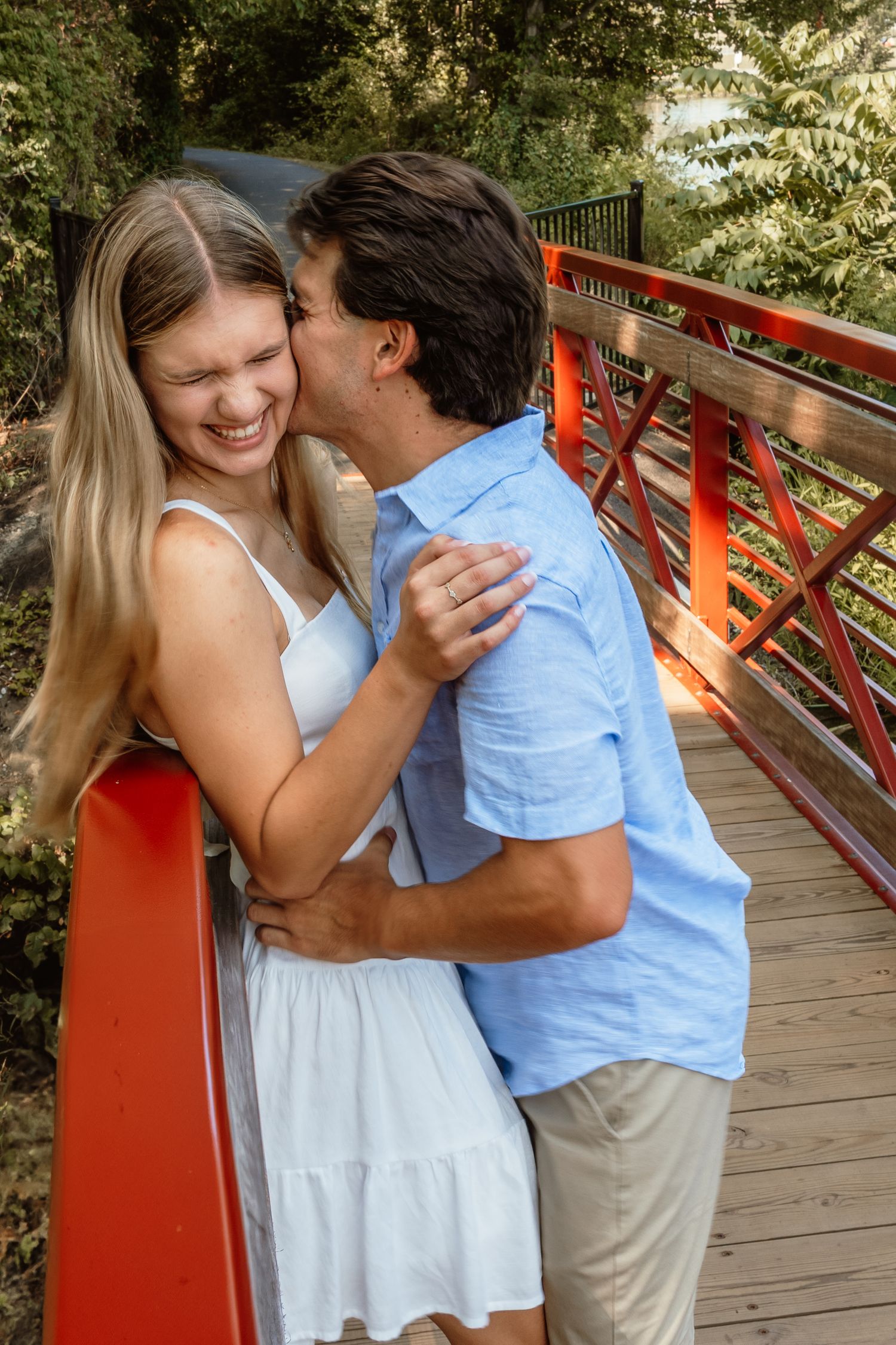 A couple shares a joyful moment together while embracing on a wooden bridge with red railings.