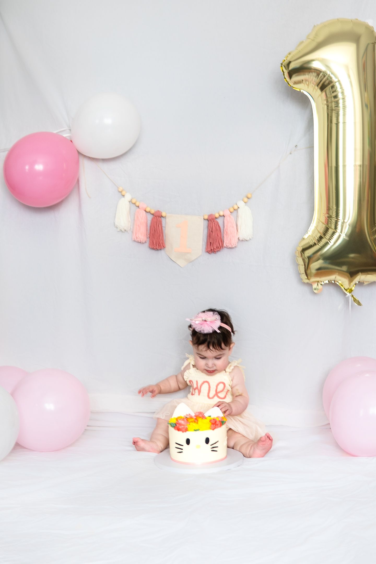 First birthday setup with Hello Kitty cake, pink balloons, and gold number one decoration.