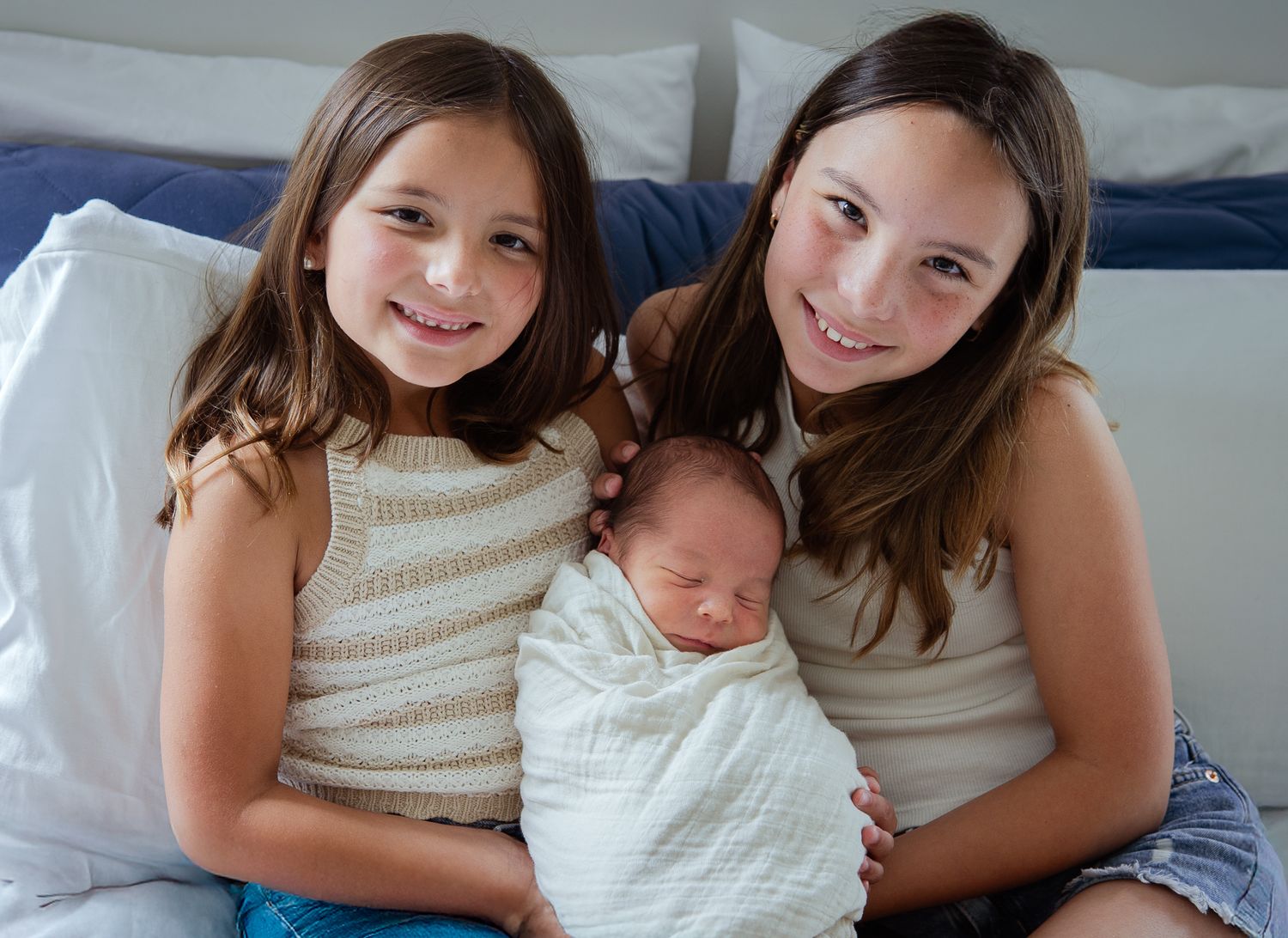 Family moment as newborn baby rests between siblings on cozy bed.
