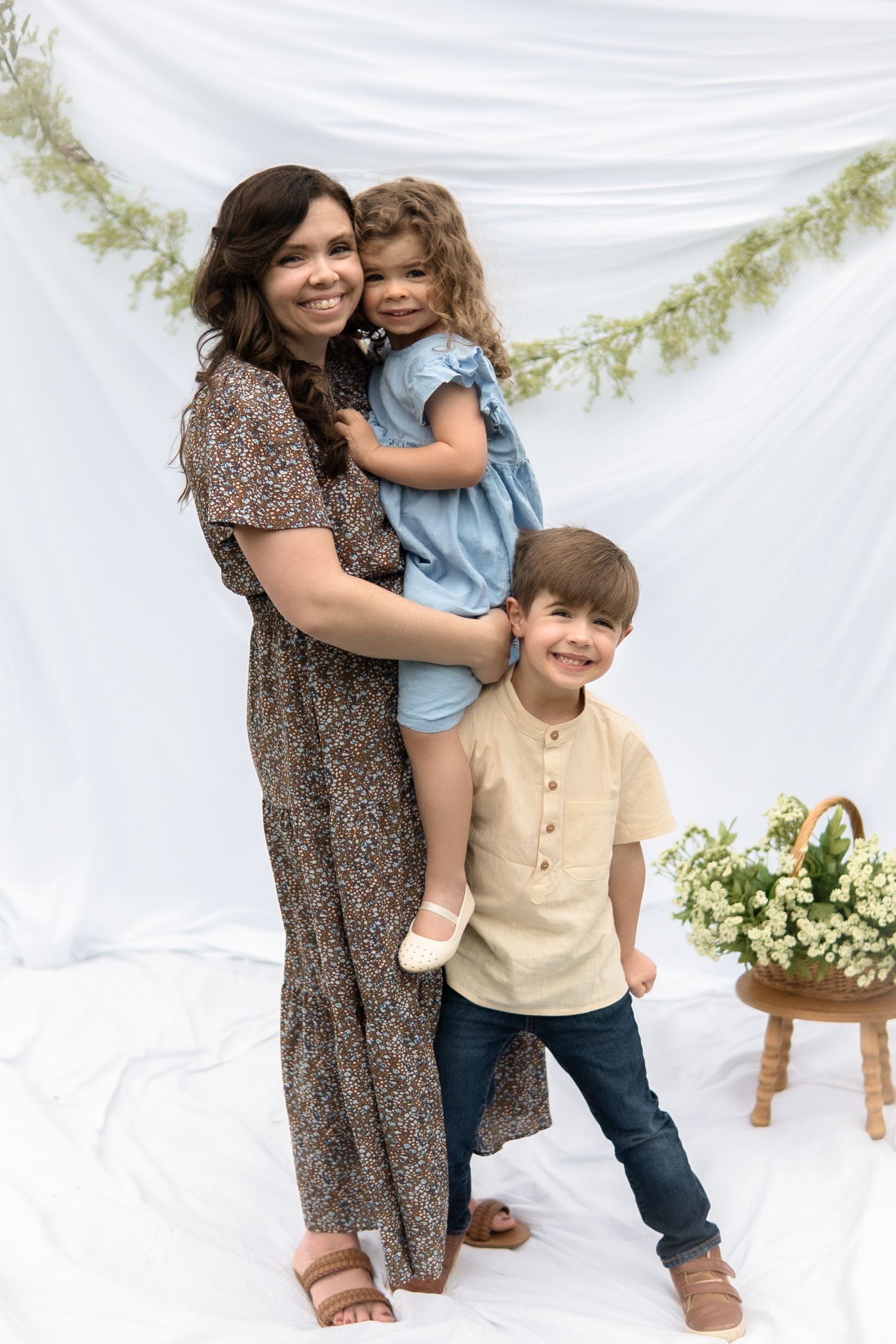 Family portrait against white backdrop with floral garland and natural decor featuring casual spring attire.