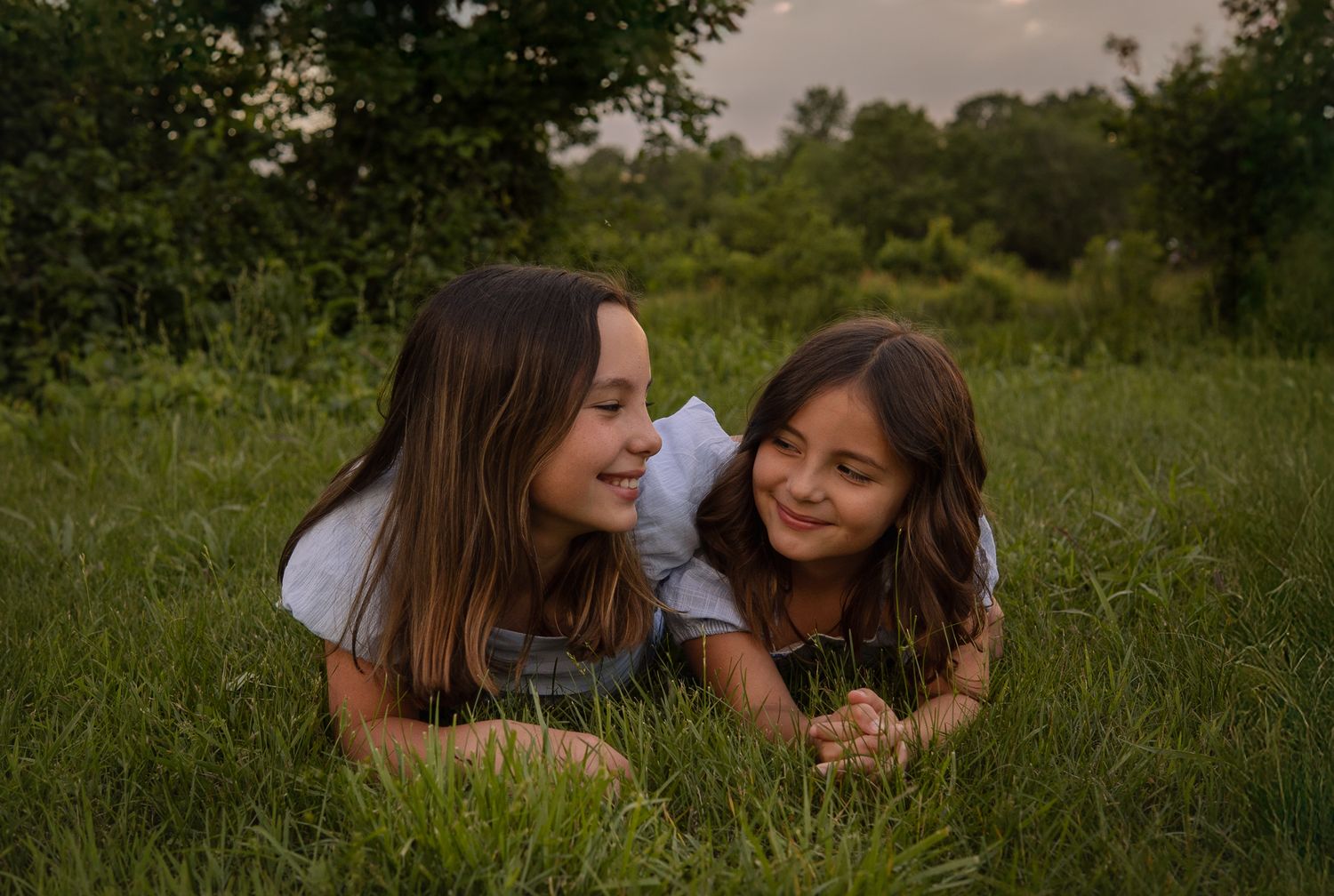 Two people laying together in a grassy field at dusk sharing a joyful moment.